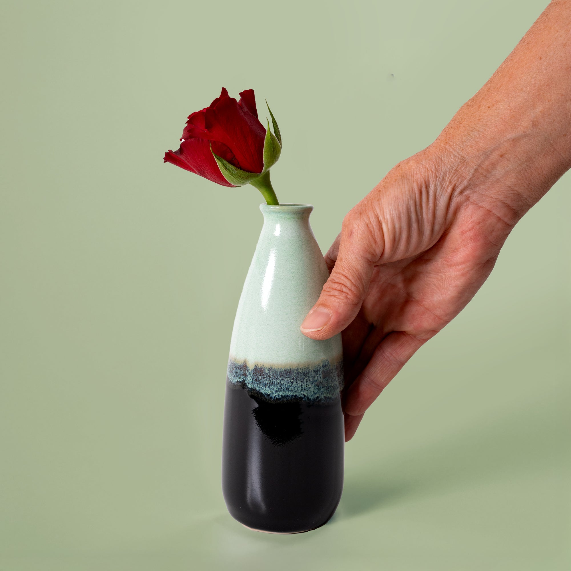 Hand holding a Pottery For The Planet artisan decorative vase for flowers with a red rose inside