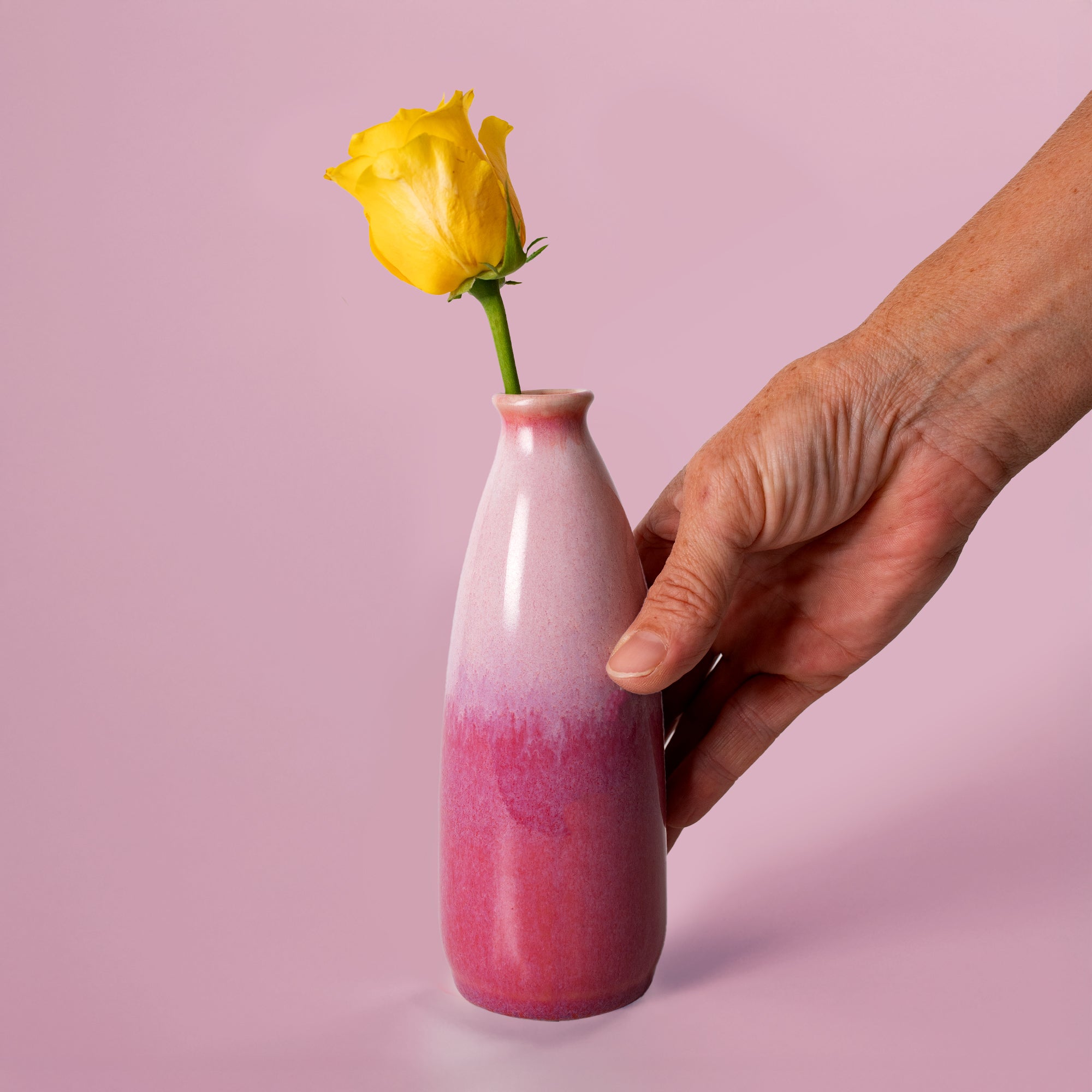 Hand holding artisan decorative vase for flowers in pink gradient with yellow rose