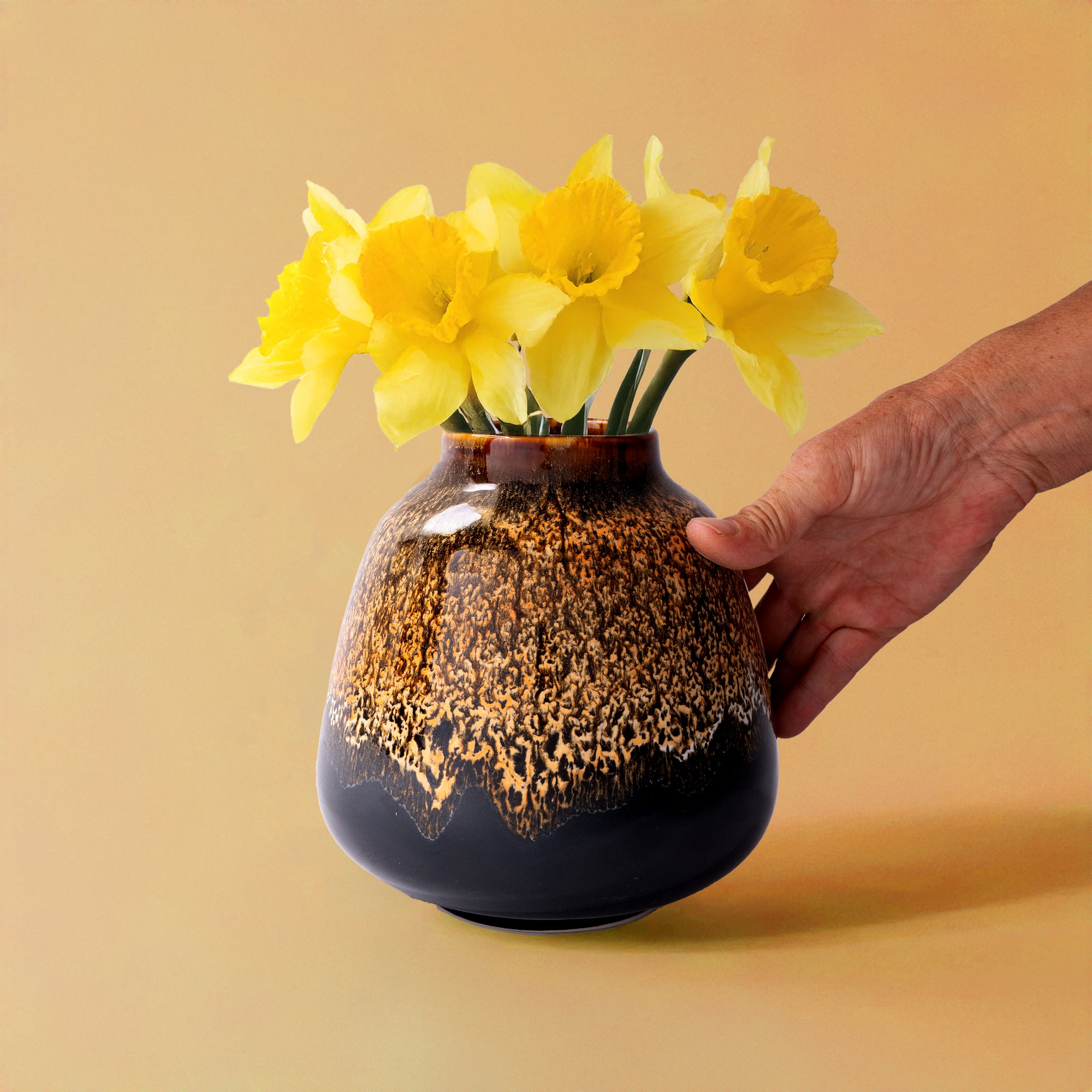 Bouquet vase for home decor in brown and black pottery with yellow daffodils being held by a hand