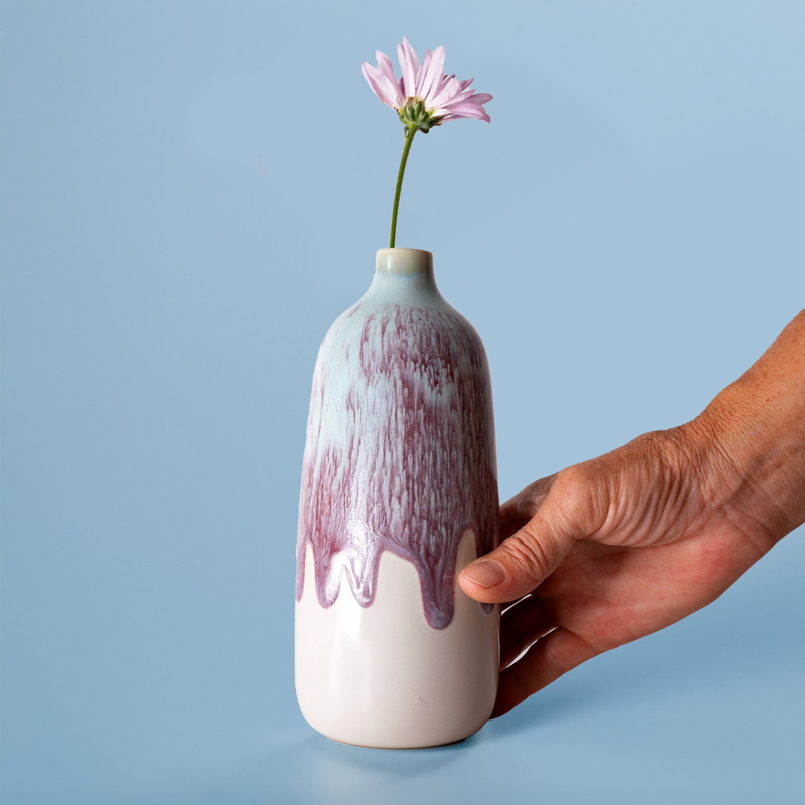 Hand holding eco-friendly home decor vase with purple and white glaze and a single pink flower
