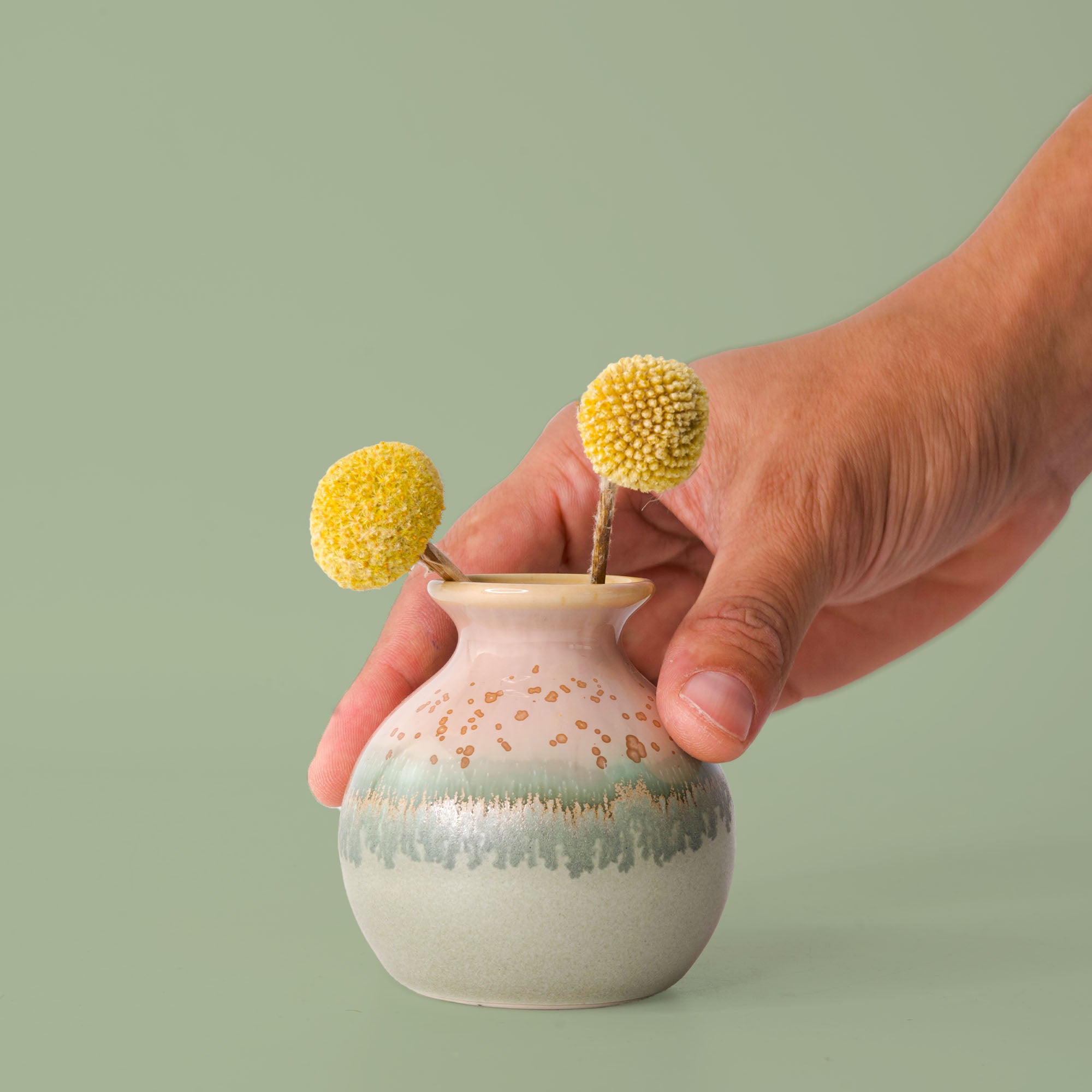 Pottery For The Planet eco-friendly home decor vase with green and beige glaze held by hand with yellow flowers