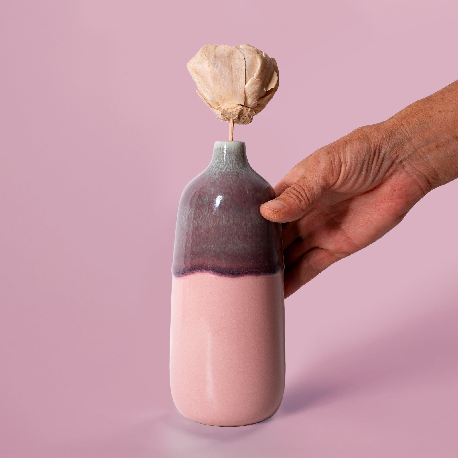 Pottery For The Planet eco-friendly home decor vase in pink and purple held by hand with dried flower