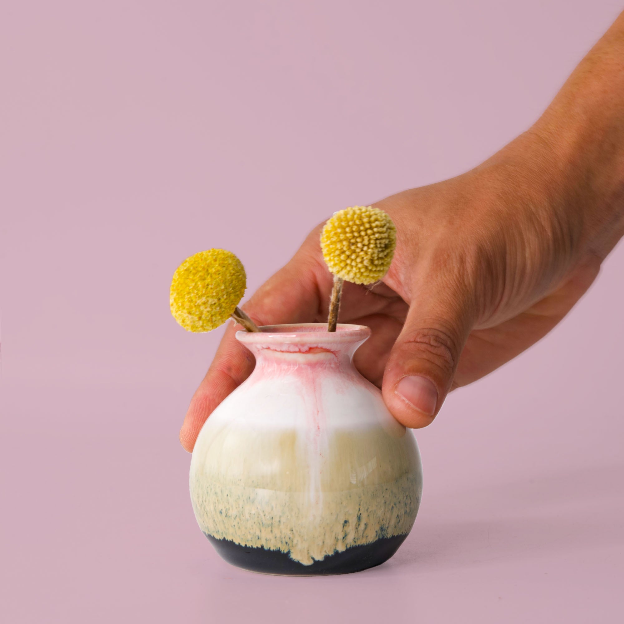 Hand holding a small eco-friendly home decor vase by Pottery For The Planet with yellow dried flowers