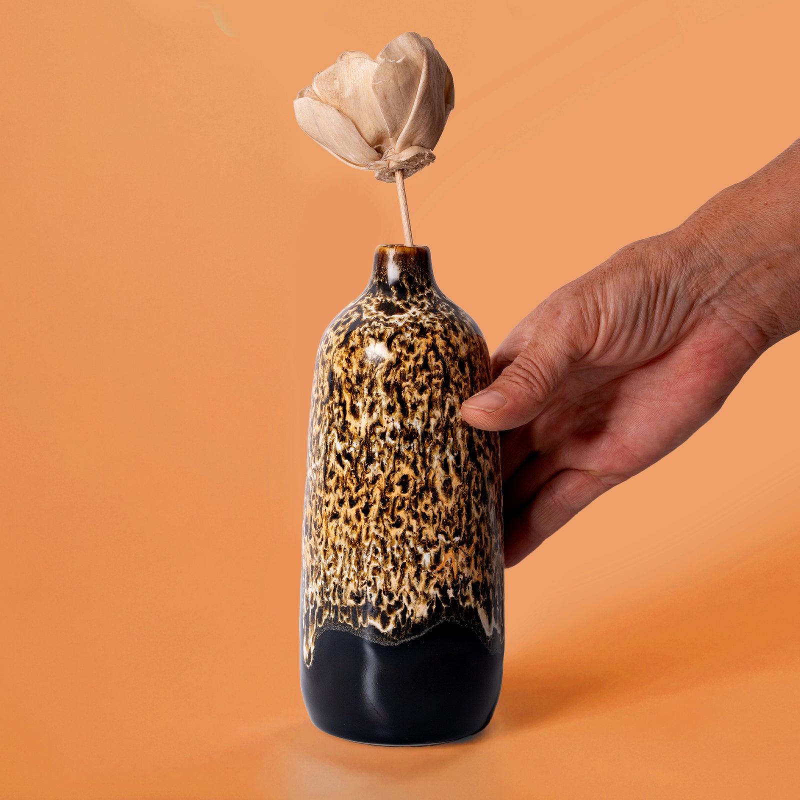 Hand holding Pottery For The Planet eco-friendly home decor vase with brown and black speckled glaze