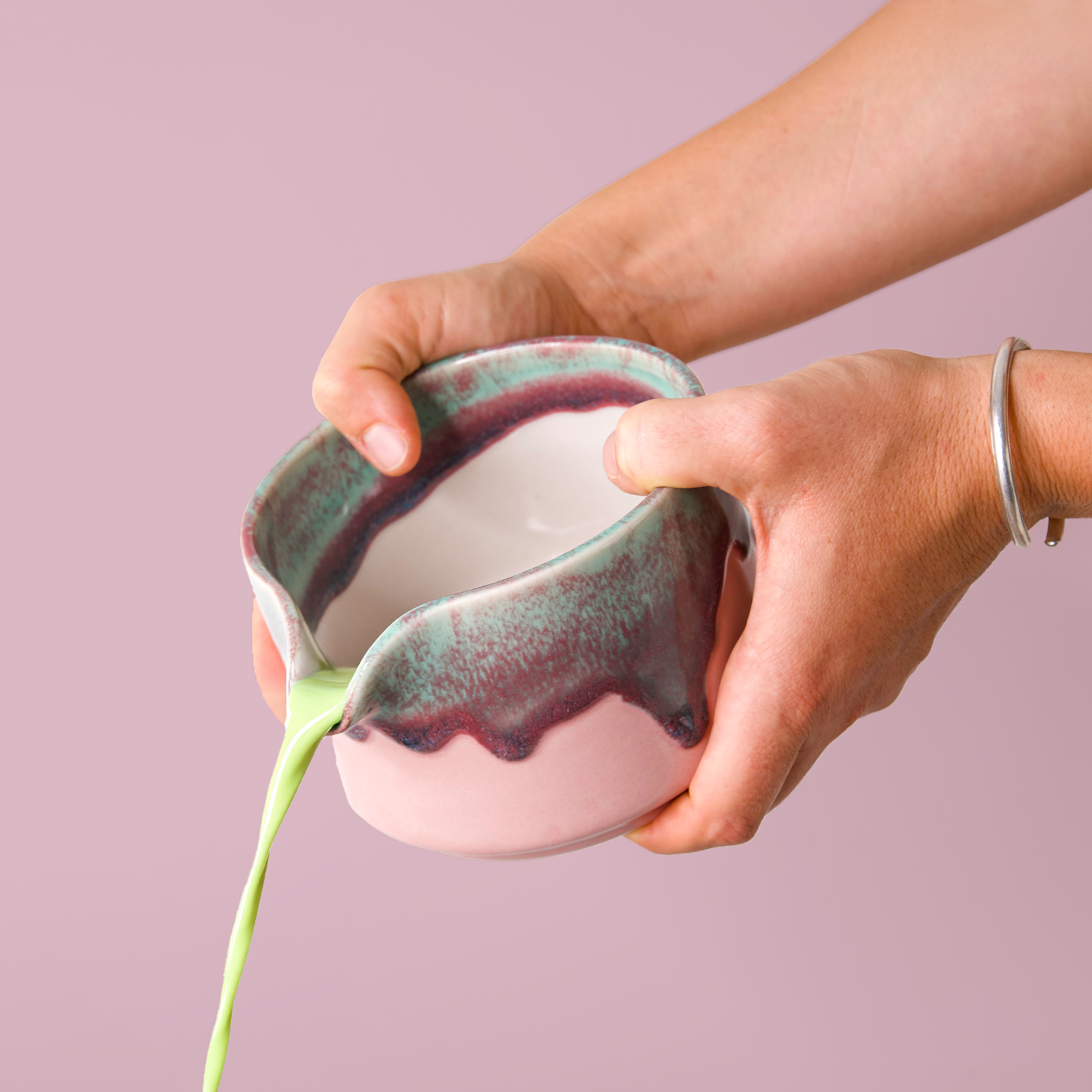 Hands pouring green tea from a handcrafted matcha bowl by Pottery For The Planet with unique glaze design