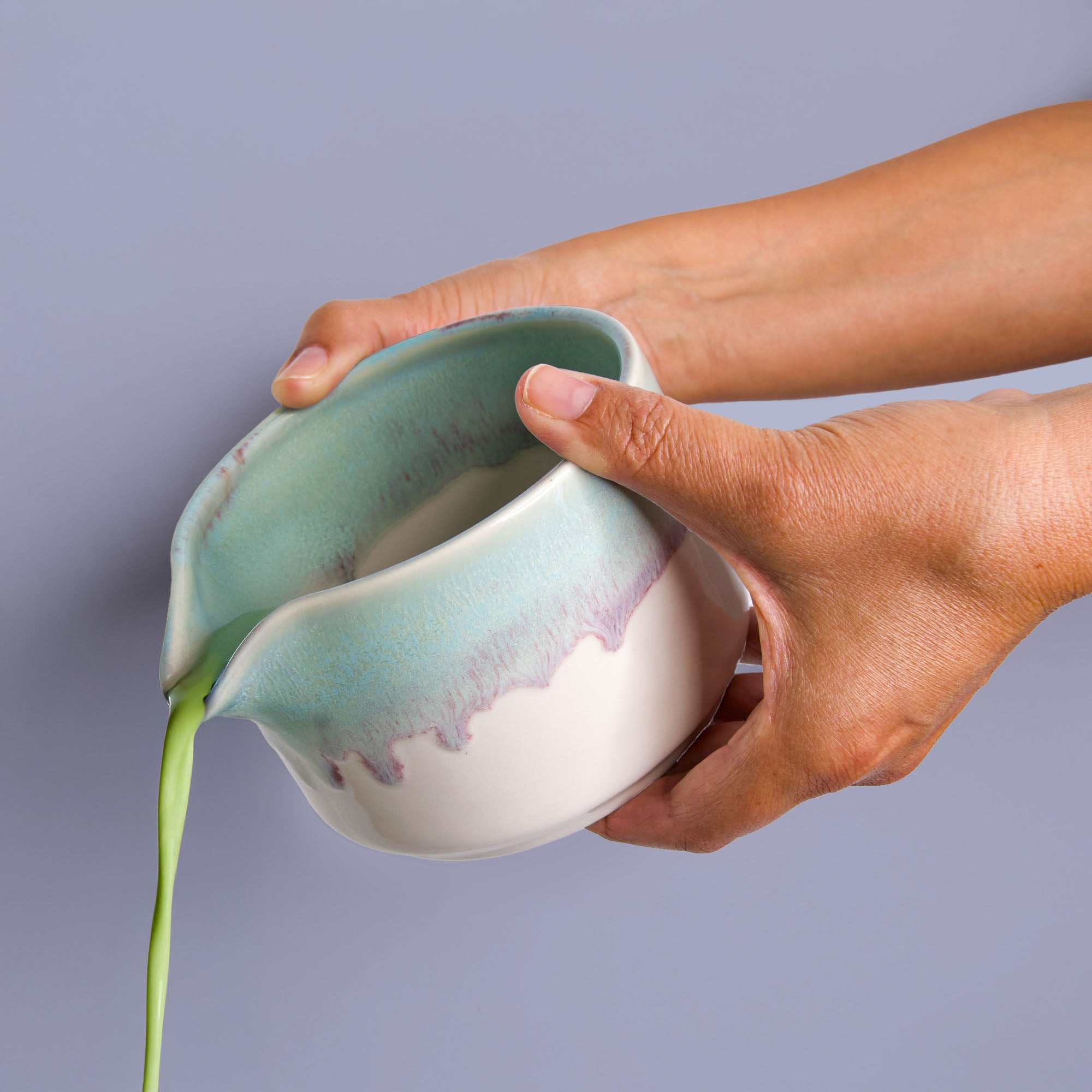 Hand pouring green tea from a handcrafted matcha bowl with a blue and white glaze by Pottery For The Planet