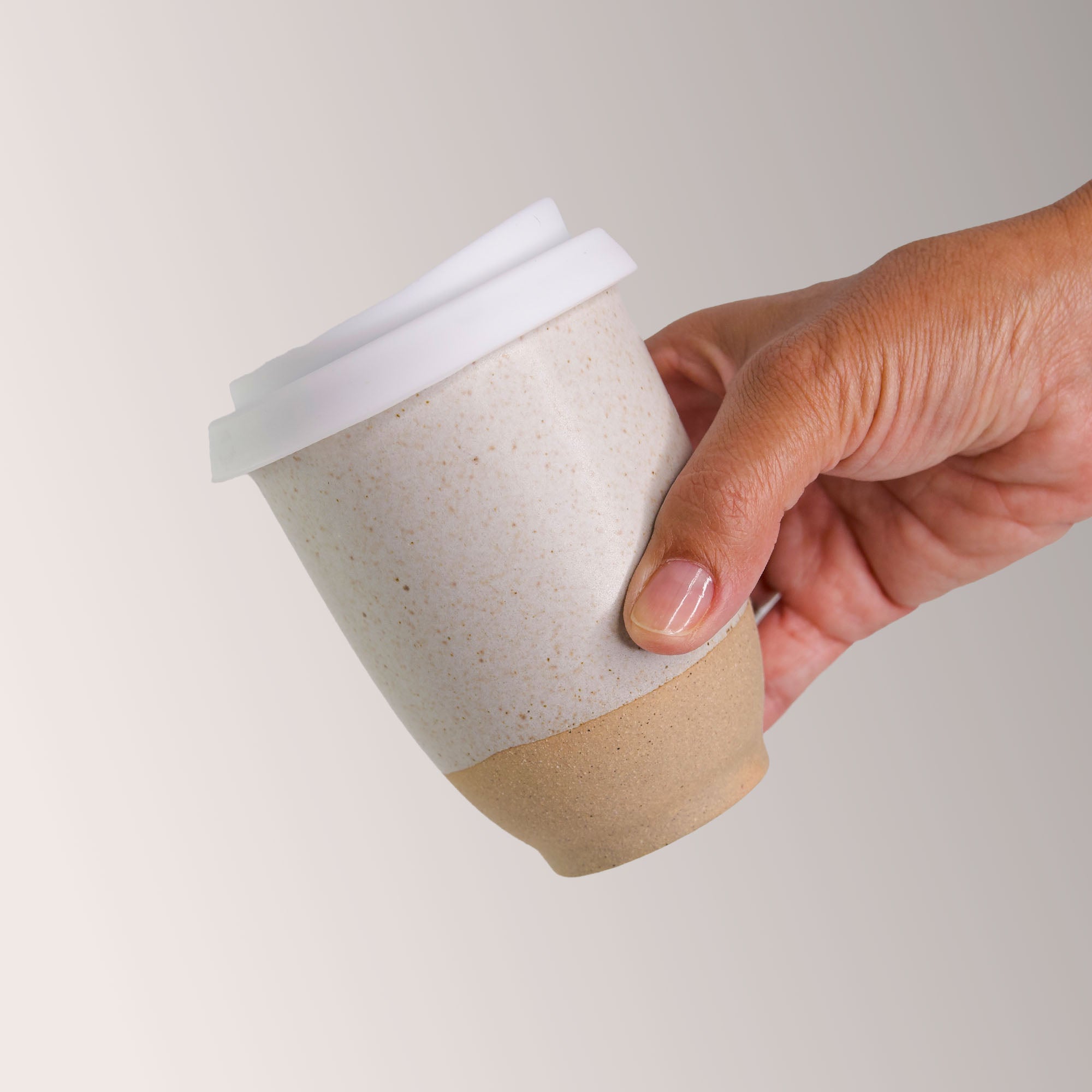 Hand holding a Pottery For The Planet handmade reusable coffee cup with white lid and earthy textured design