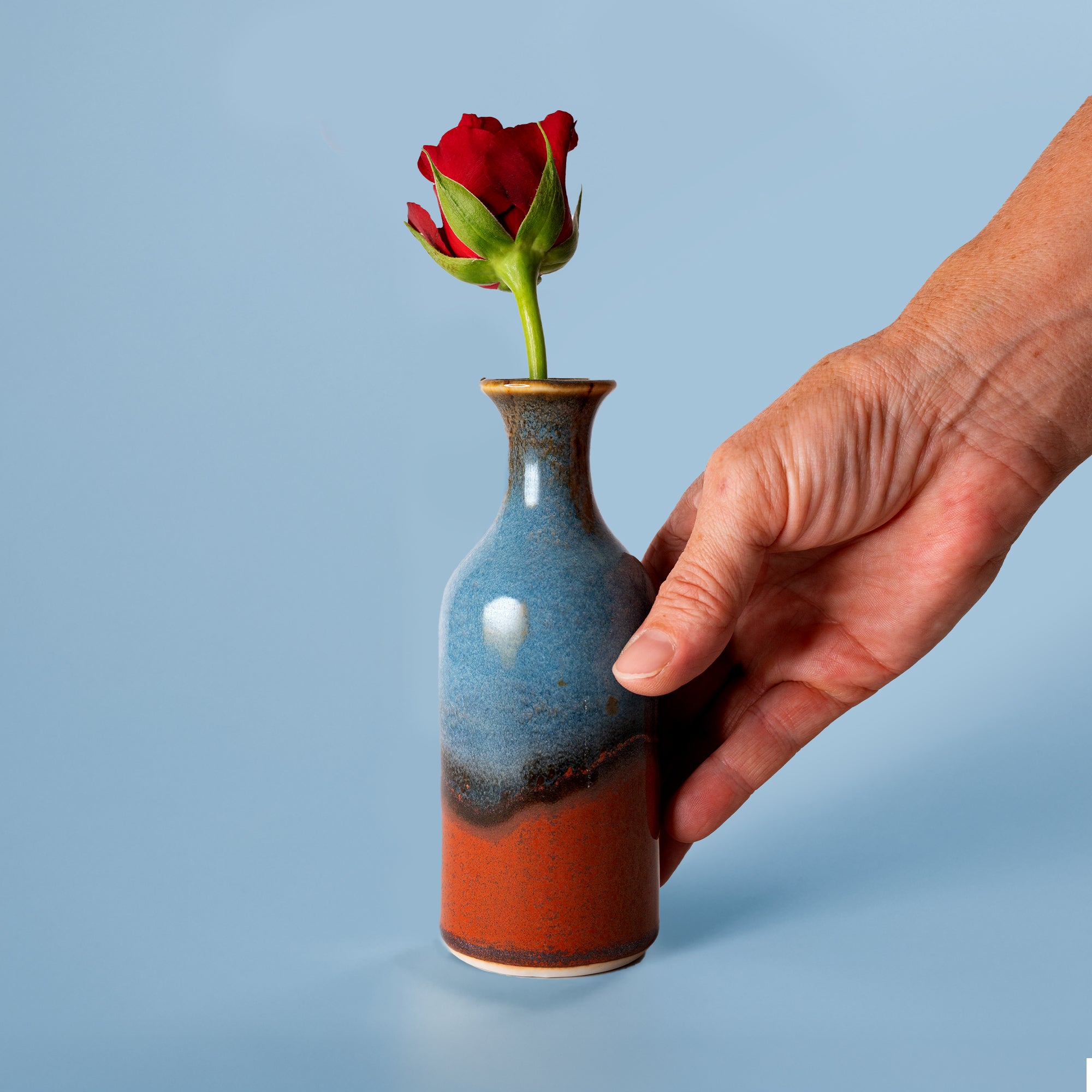 Pottery For The Planet small handmade flower vase in blue and rust colors holding a single red rose