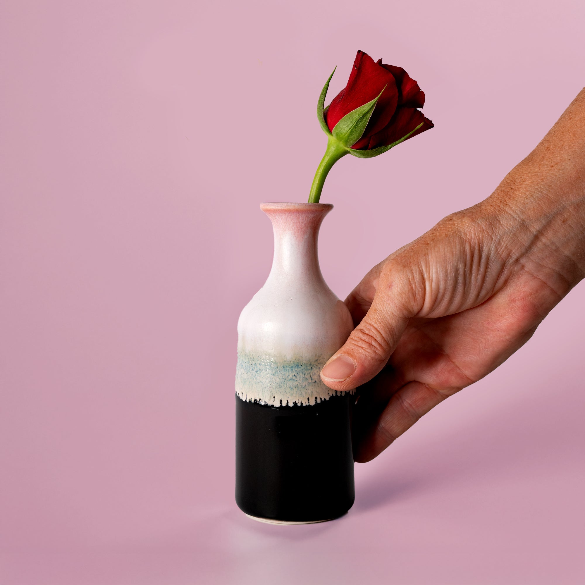 Small handmade flower vase by Pottery For The Planet holding a single red rose with a hand holding it