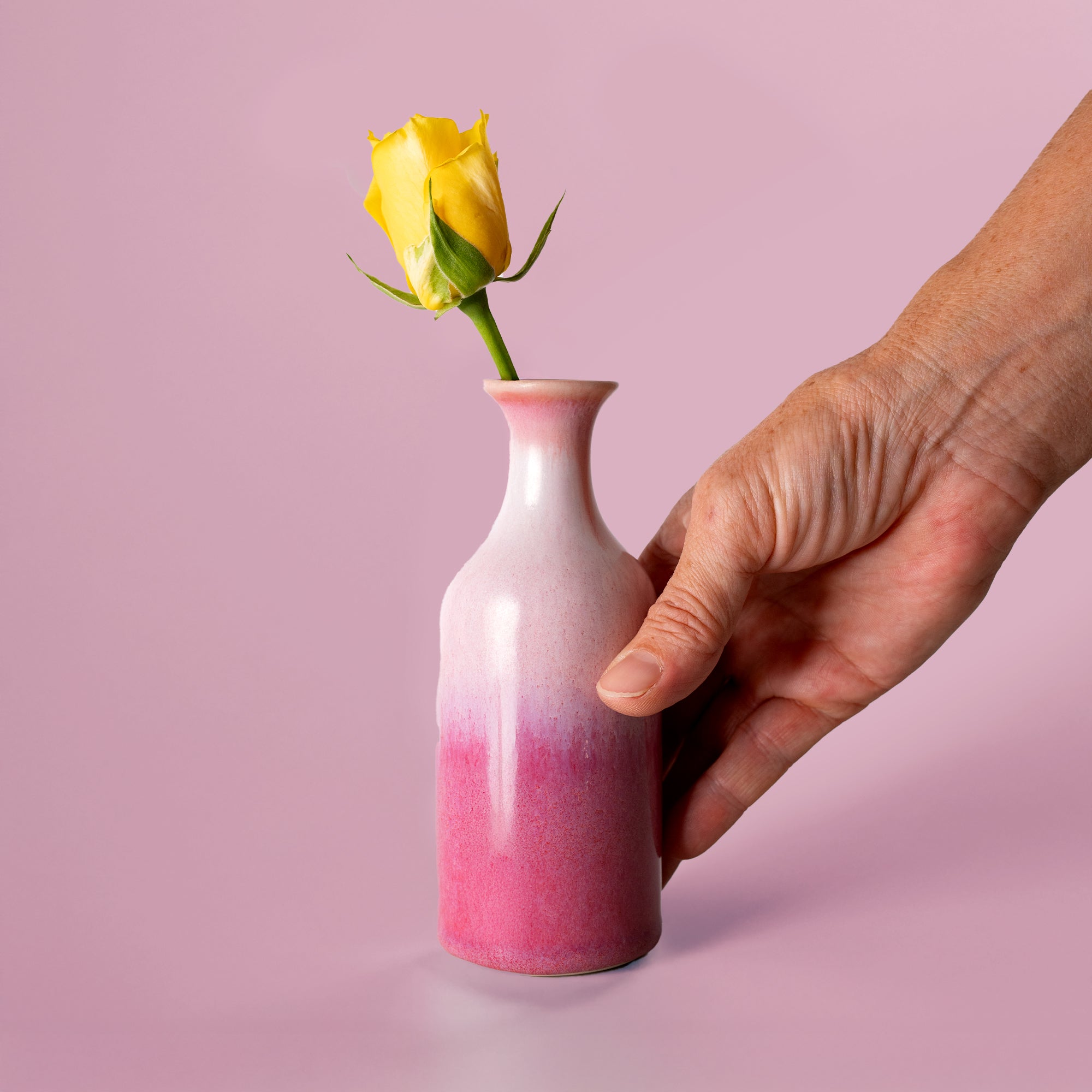 Pottery For The Planet small handmade flower vase in pink gradient with single yellow rose held by hand