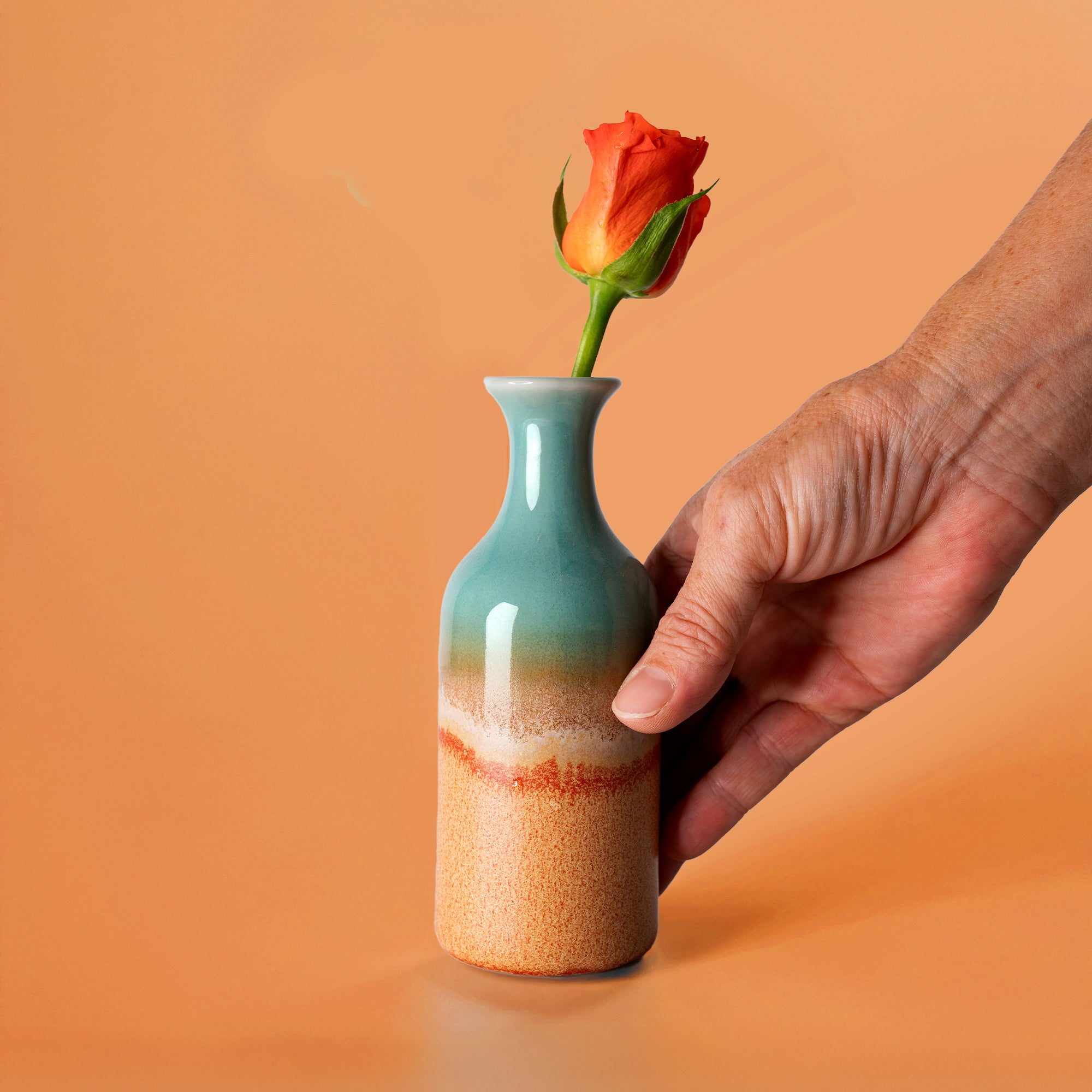 Pottery For The Planet small handmade flower vase with blue and orange glaze holding a single orange rose
