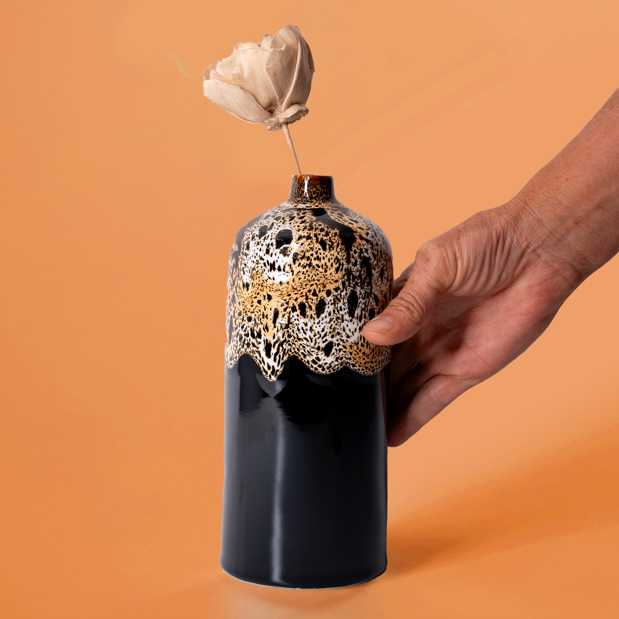 Pottery For The Planet medium decorative bud vase with black and gold textured design held by hand with dried flower