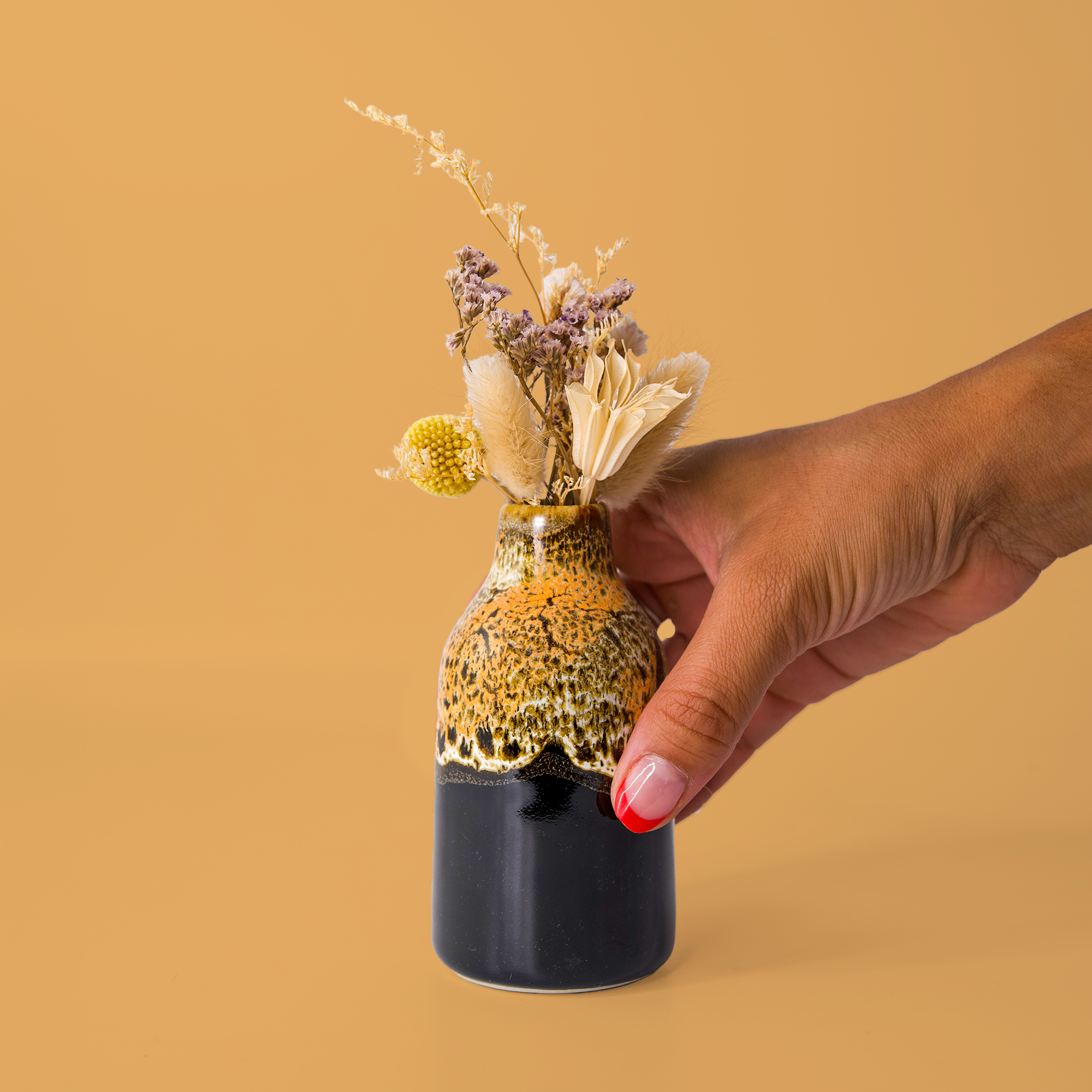 Hand holding Pottery For The Planet modern decorative flower vase with dried flowers on beige background