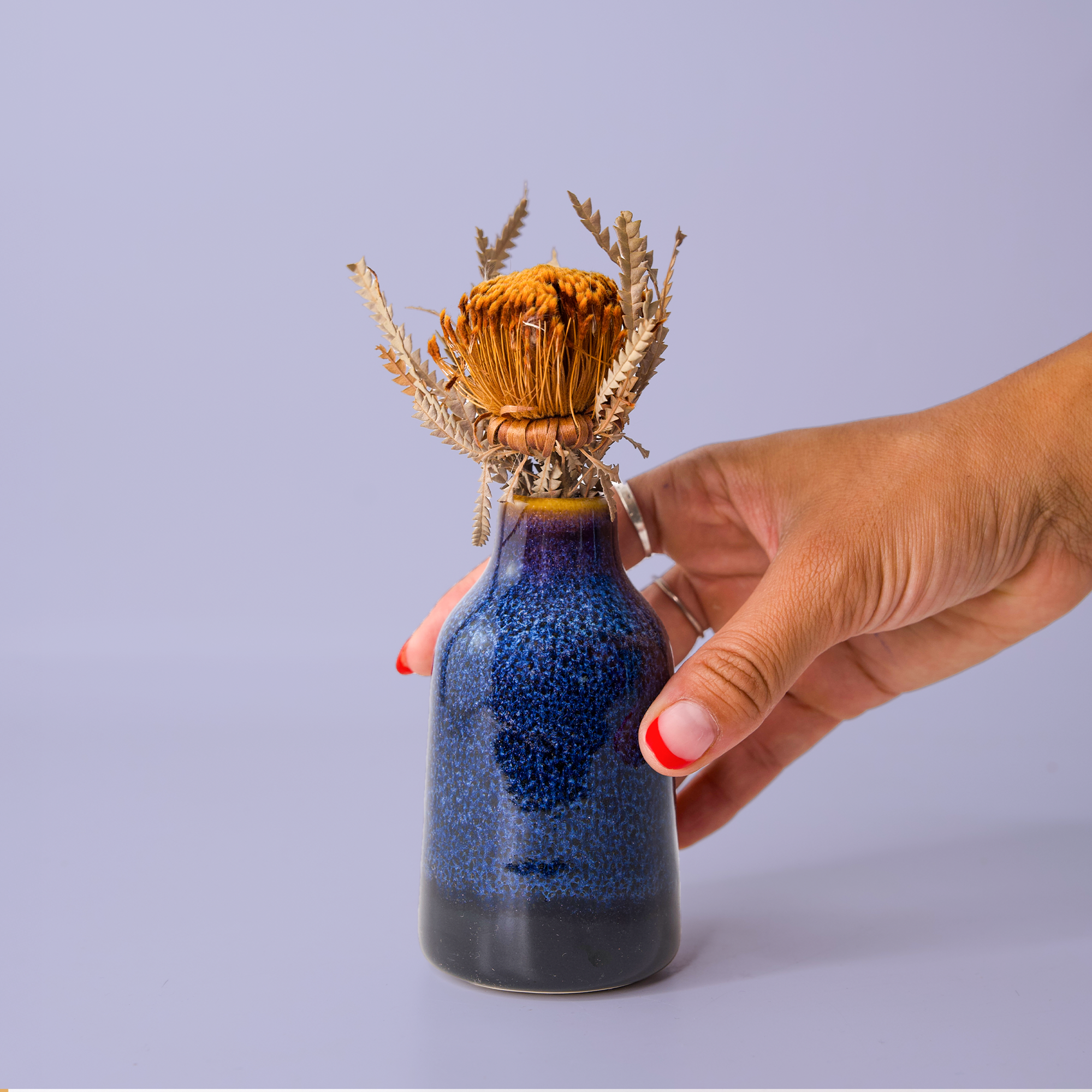 Hand holding a Pottery For The Planet modern decorative flower vase with blue glaze and dried flowers