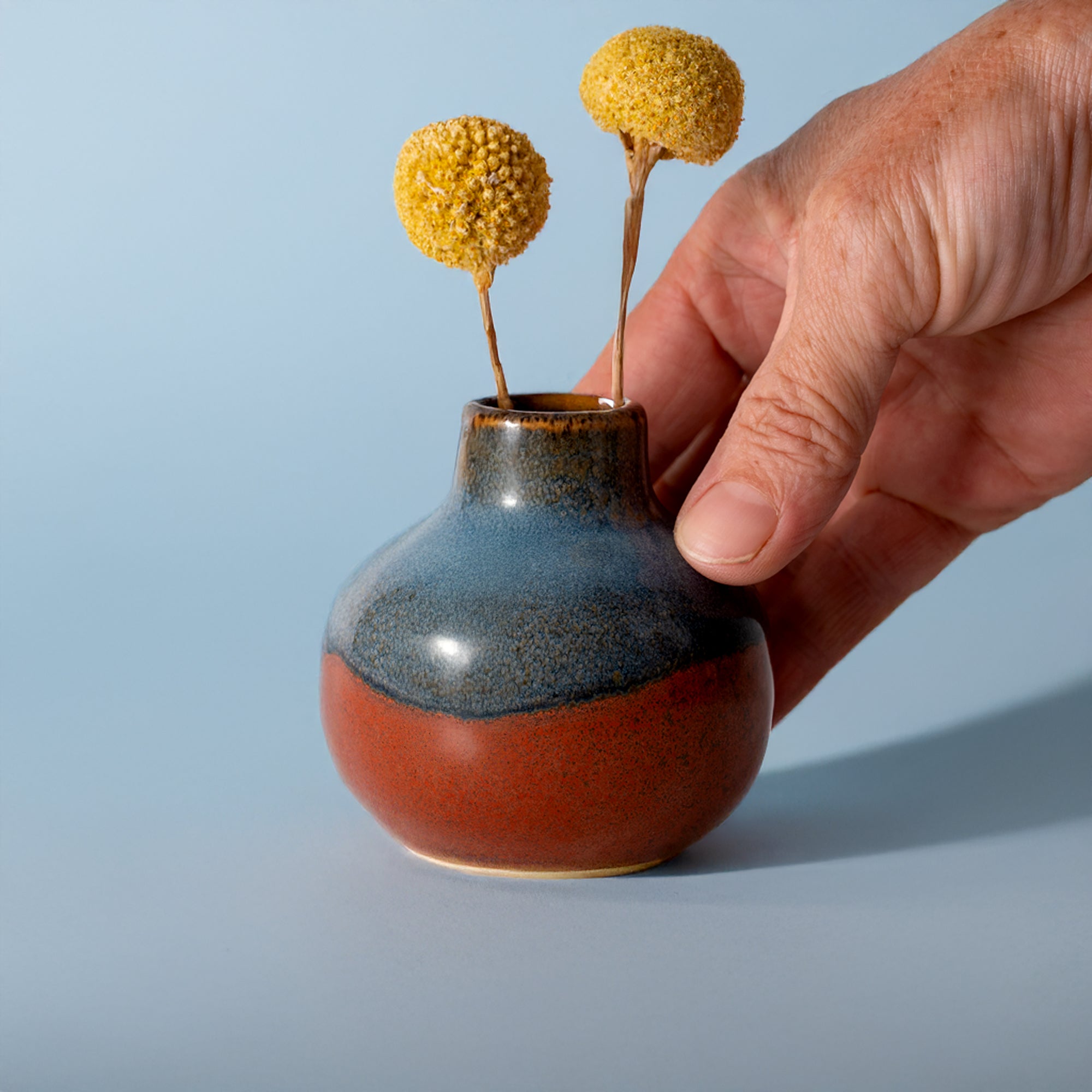 Pottery For The Planet small handmade home decor vase with blue and red glaze held by hand with yellow dried flowers