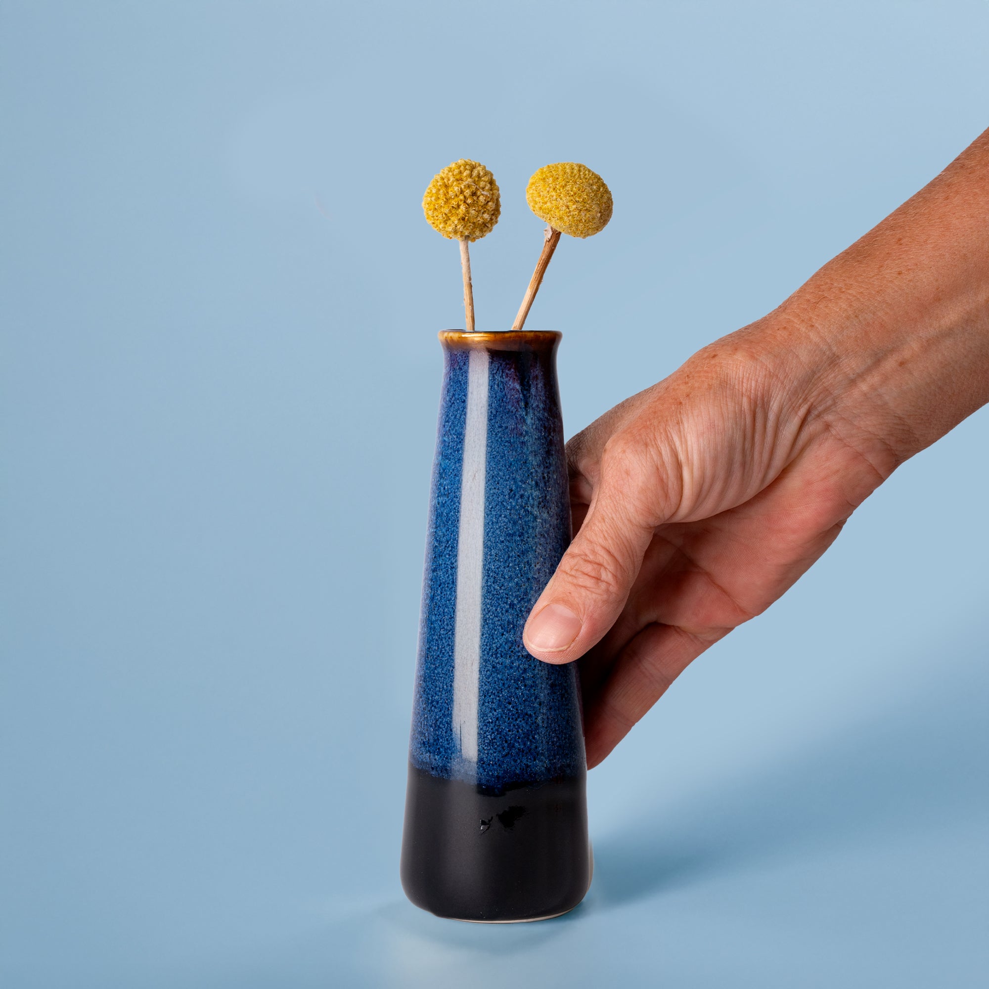 Blue and black Pottery For The Planet sustainable home decor vase held by hand with yellow billy ball flowers