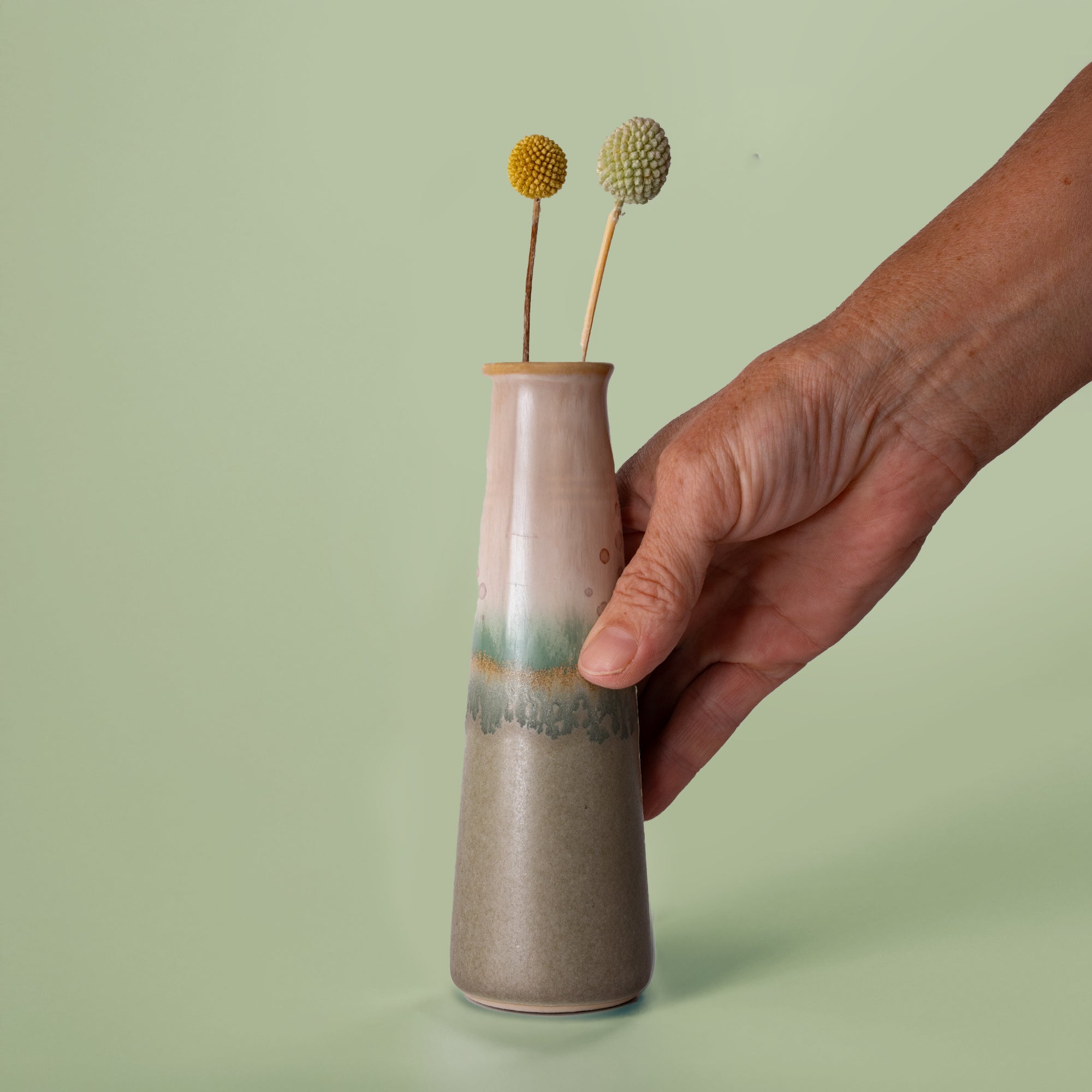 Hand holding a Pottery For The Planet sustainable home decor vase with earthy tones and dried flowers