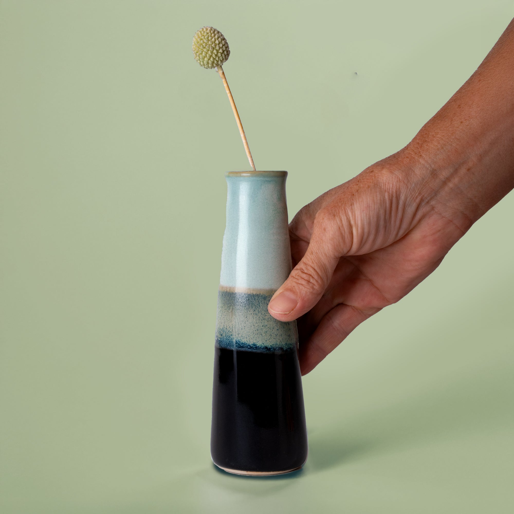 Hand holding a sustainable home decor vase with blue and black glaze from Pottery For The Planet