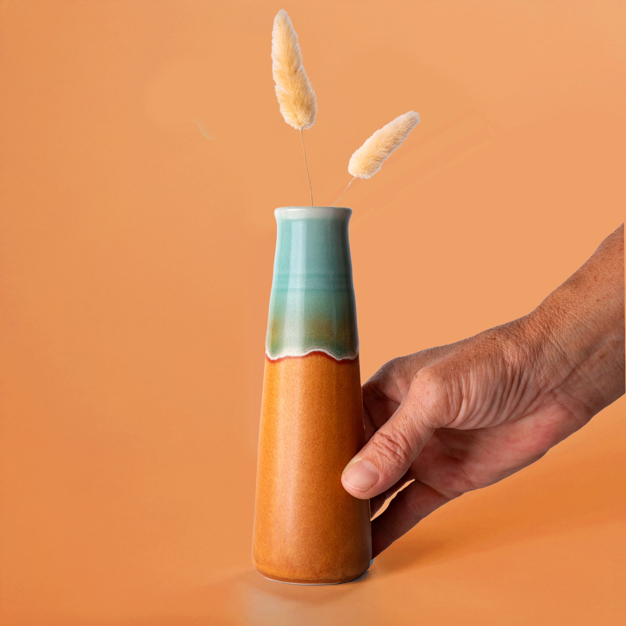 Hand holding Pottery For The Planet sustainable home decor vase with blue and brown glaze and dried flowers