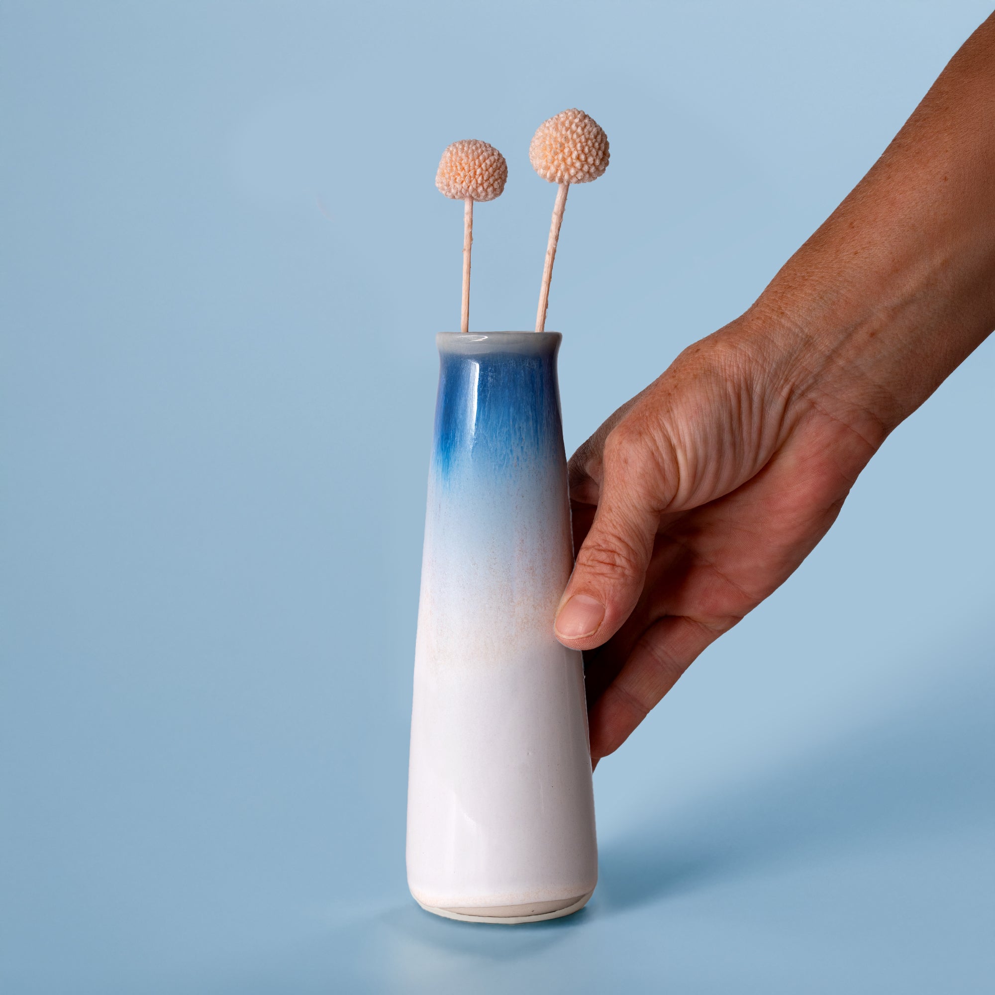 Hand holding a blue and white sustainable home decor vase by Pottery For The Planet with dried flowers