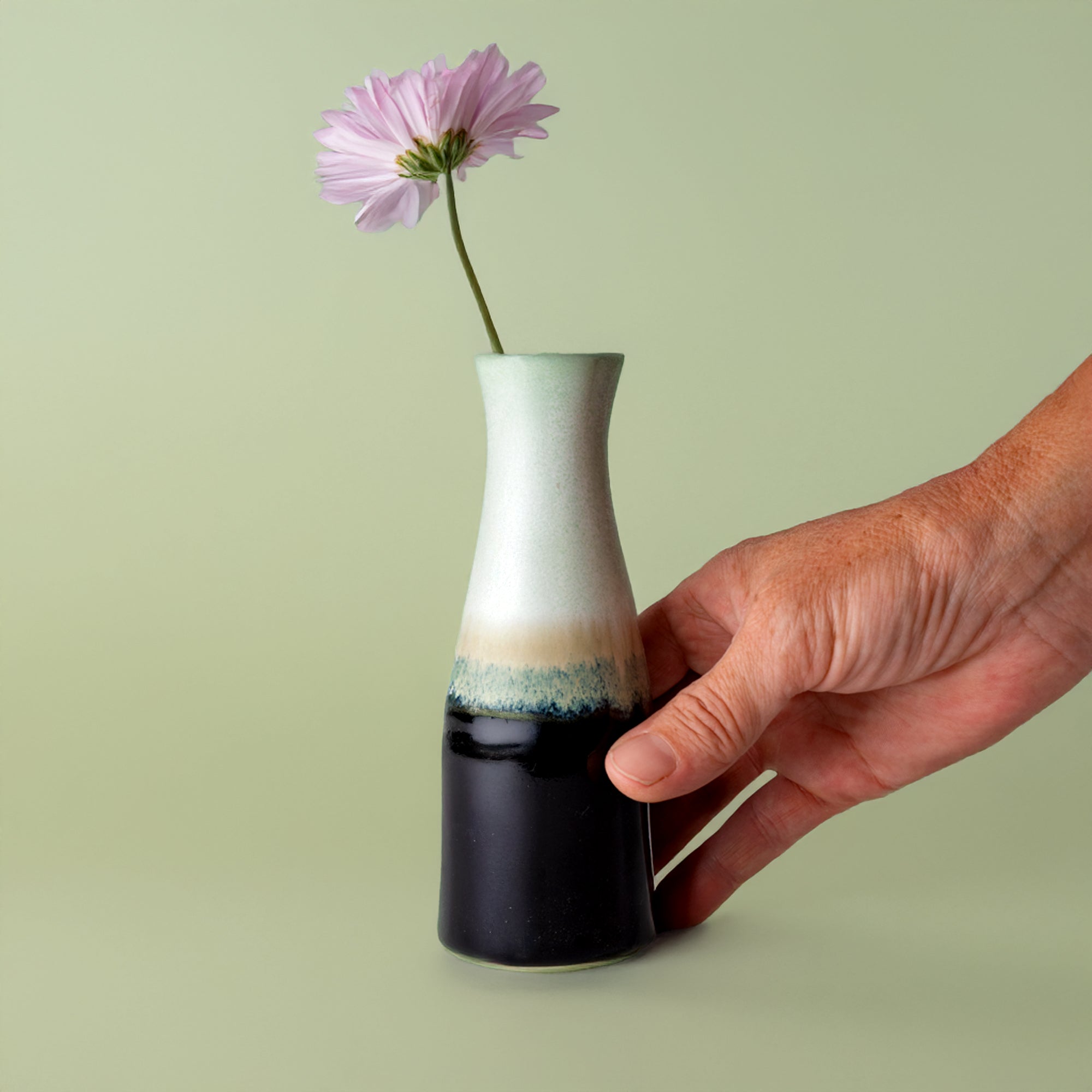 Hand holding a unique ceramic flower vase with gradient green and black glaze from Pottery For The Planet