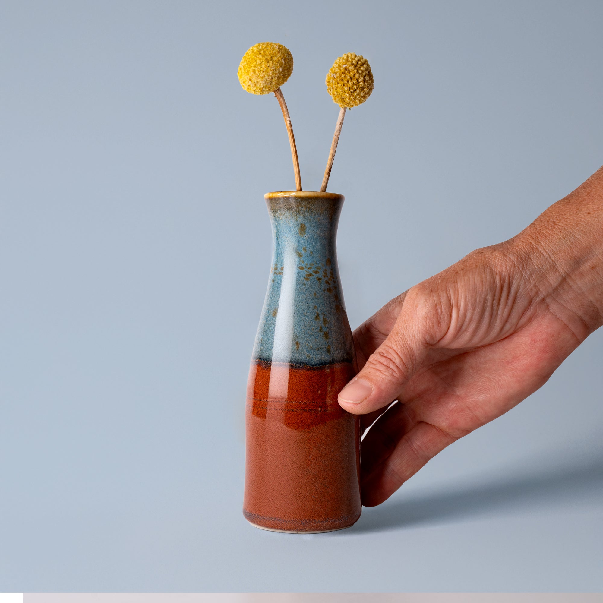 Pottery For The Planet unique ceramic flower vase in blue and brown held by hand with yellow flowers