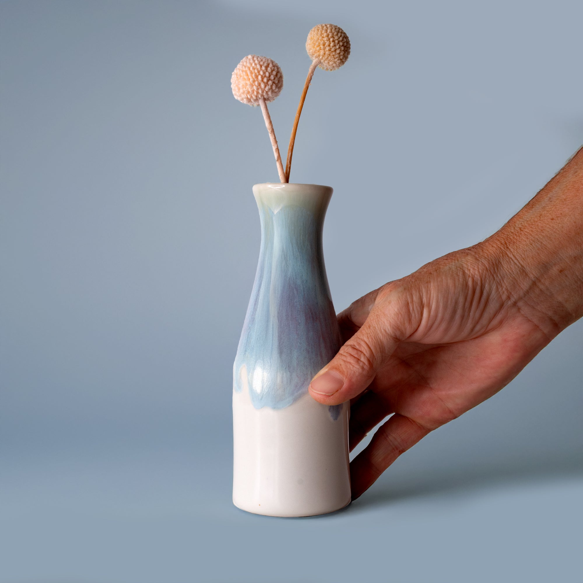 Hand holding a unique ceramic flower vase with blue and white glaze from Pottery For The Planet