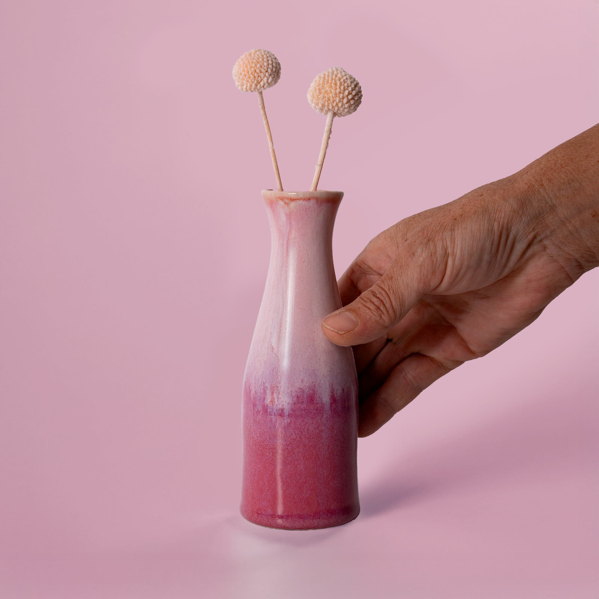 Hand holding unique ceramic flower vase in pink gradient with two decorative dried flowers