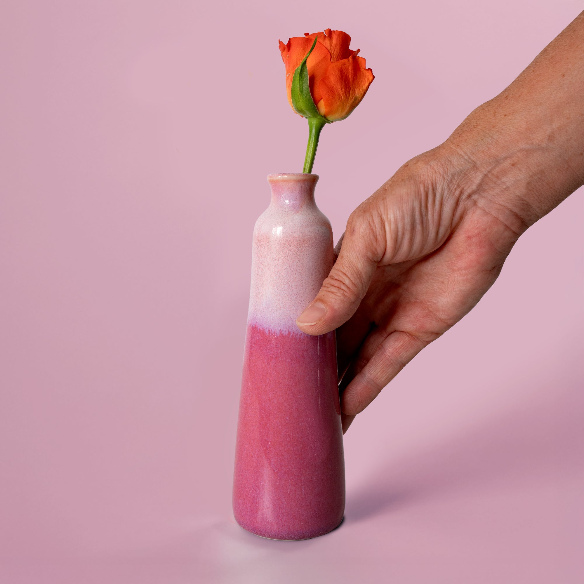 Unique handmade ceramic vase in pink gradient held by hand with an orange rose from Pottery For The Planet
