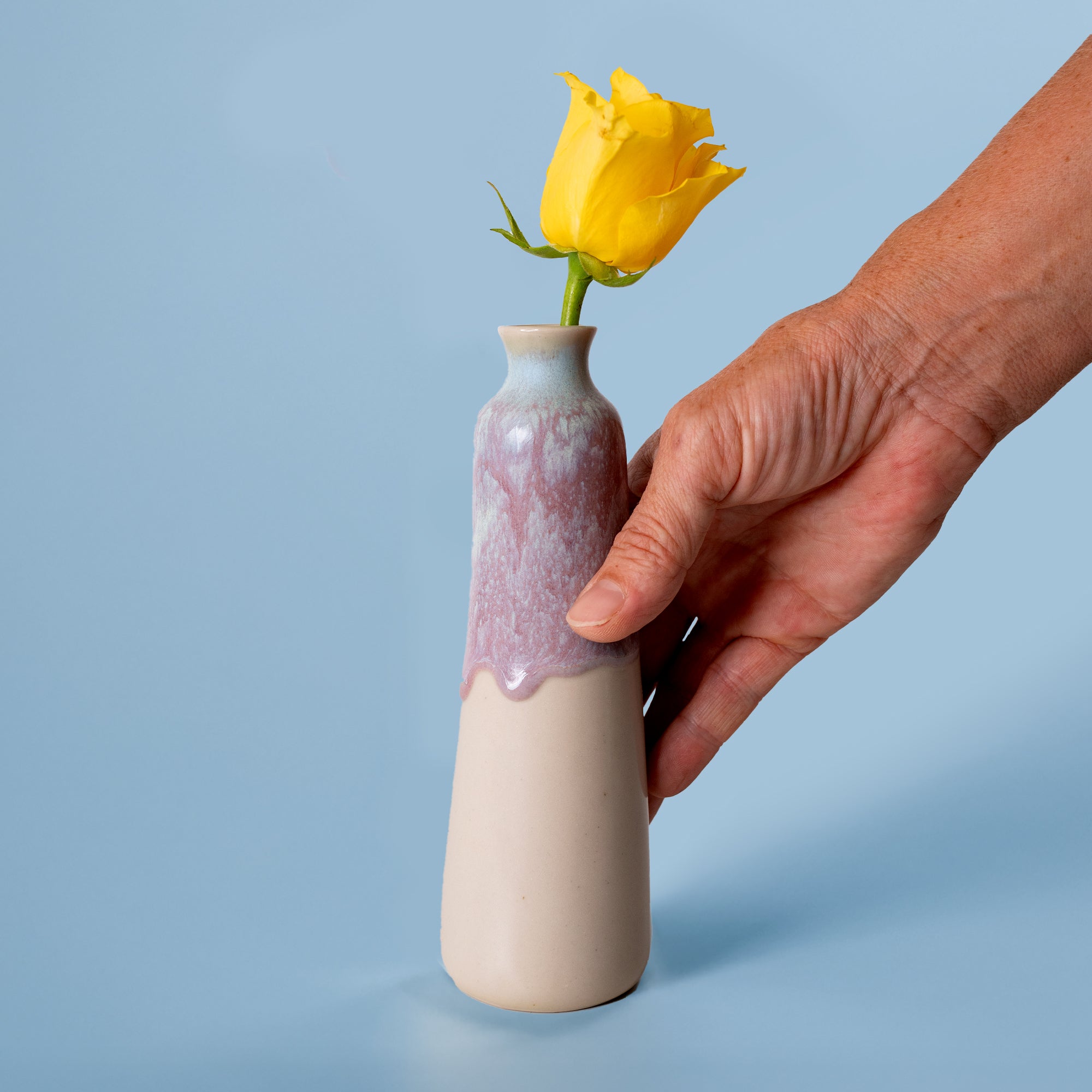 Hand holding unique handmade ceramic vase with purple glaze and yellow rose by Pottery For The Planet