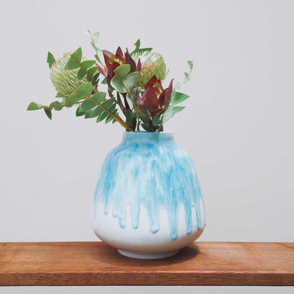 Blue and white ceramic bouquet vase for home decor with green leaves and flowers on wooden surface