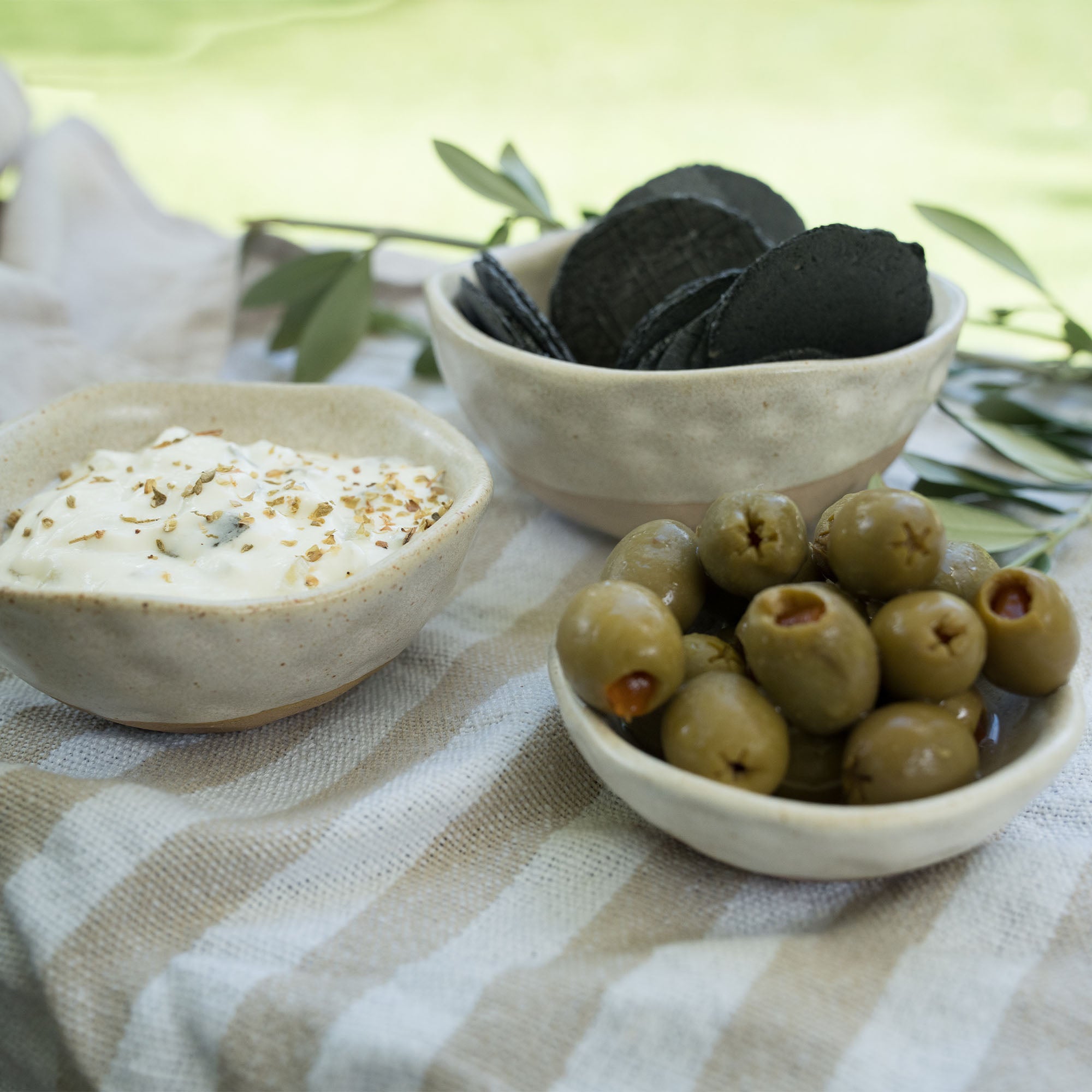Nesting dishes in sandy glaze displayed with crackers, cheese and olives. 