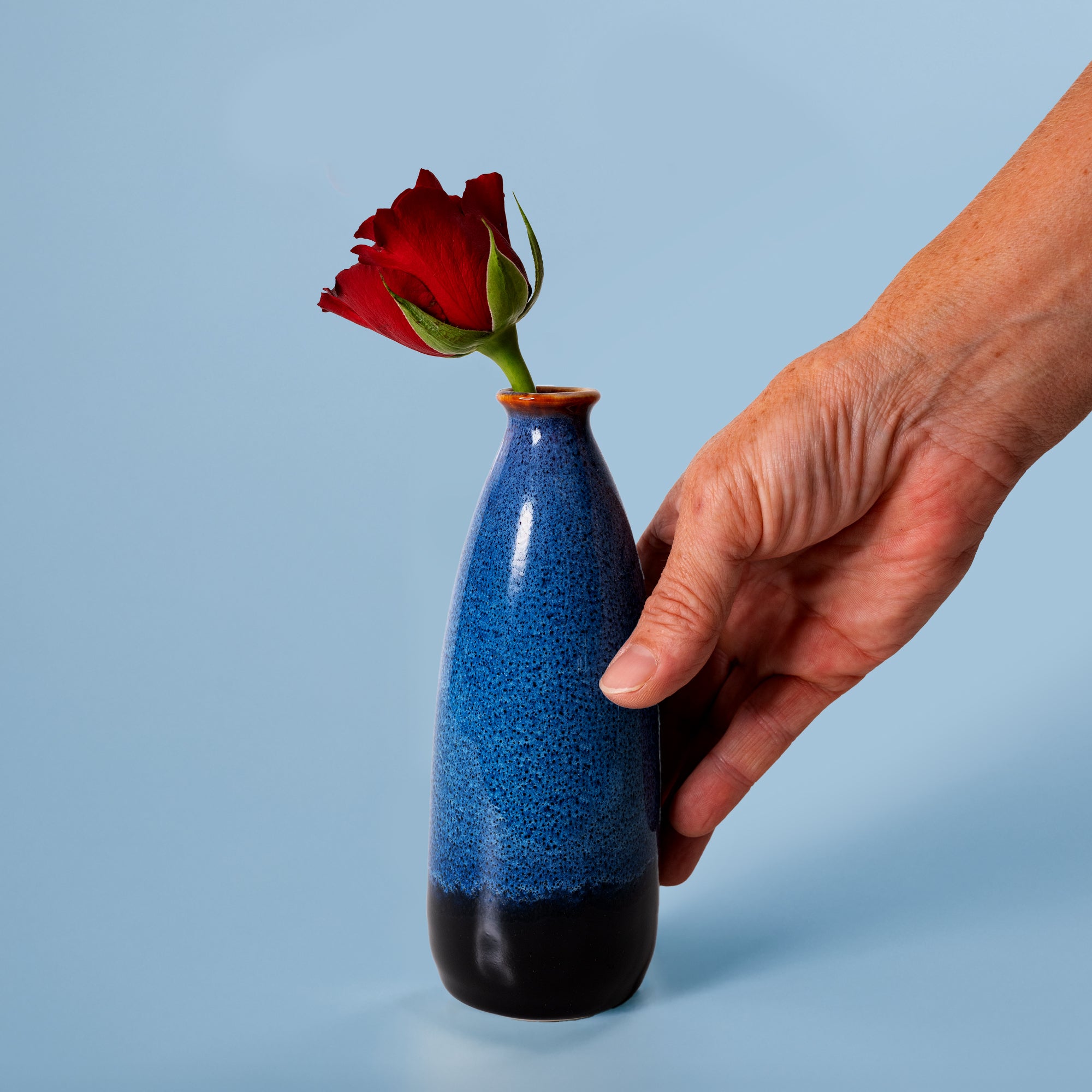 Hand holding blue and black artisan decorative vase for flowers with a single red rose