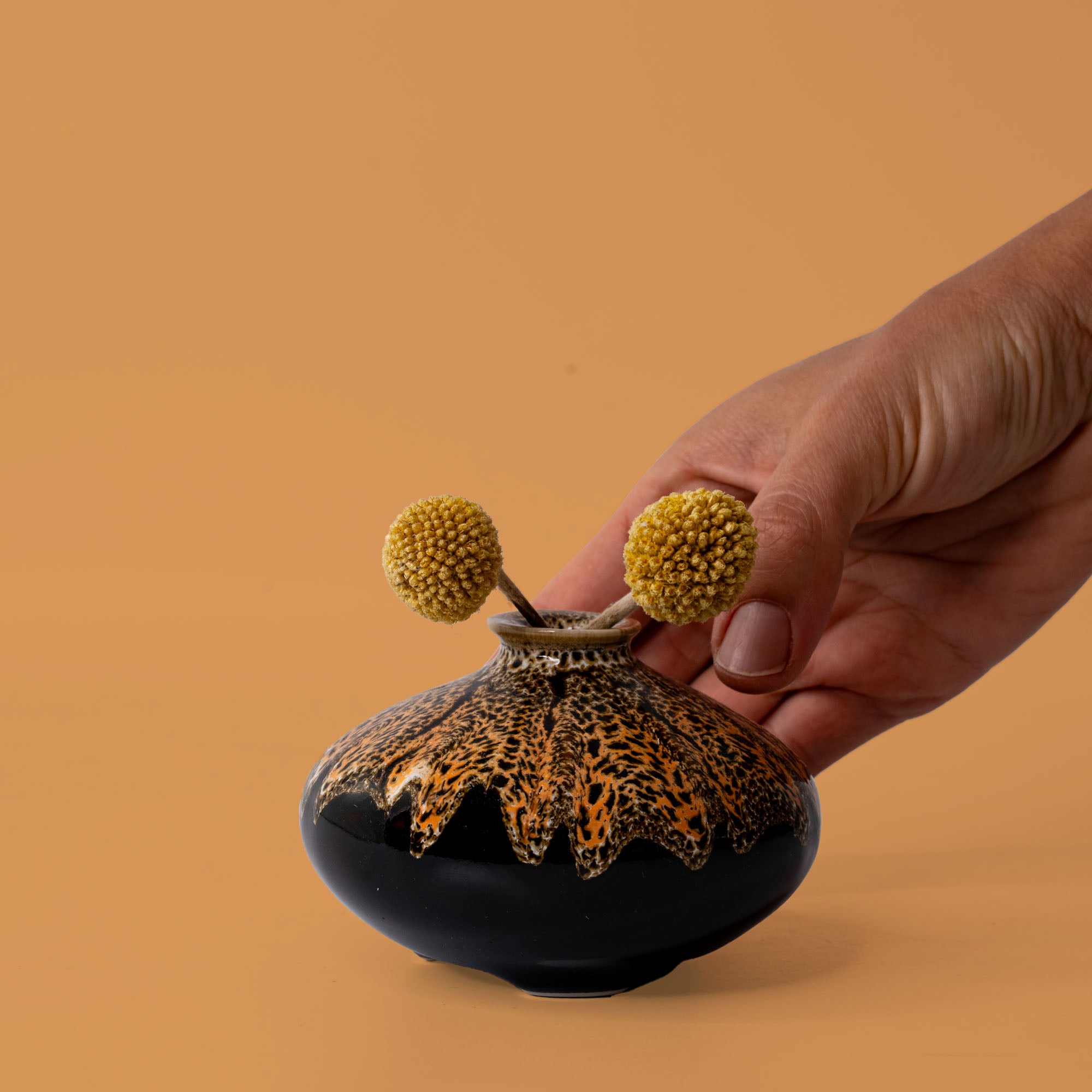 Hand holding a small black and orange handcrafted vase with two yellow billy ball flowers artisan decorative vases
