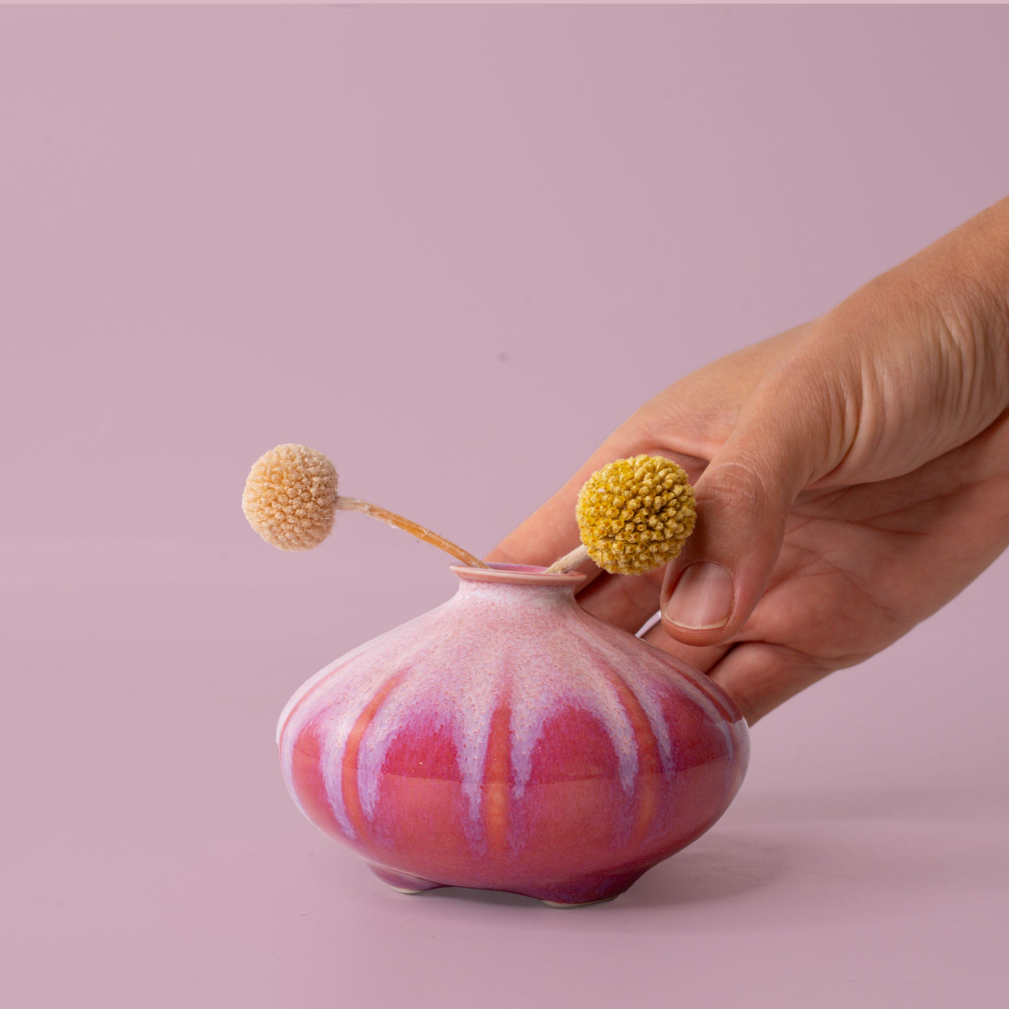 Hand holding pink artisan decorative vases with unique glaze and dried flowers