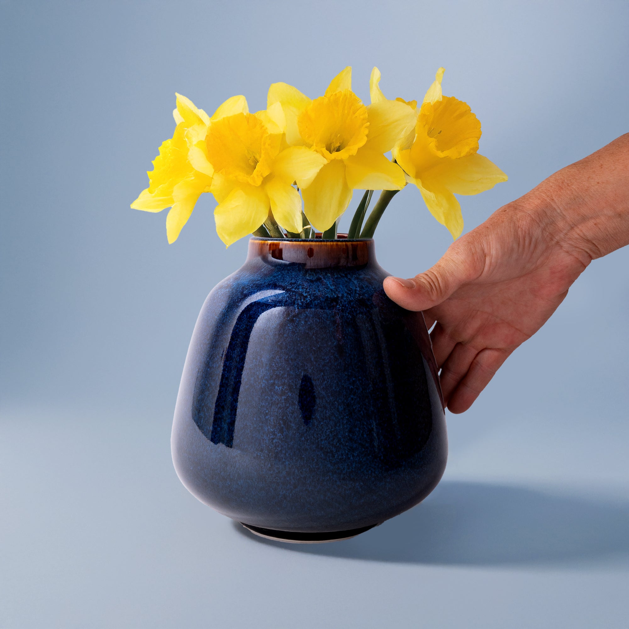 Pottery For The Planet blue bouquet vase for home decor holding yellow daffodils with hand beside it