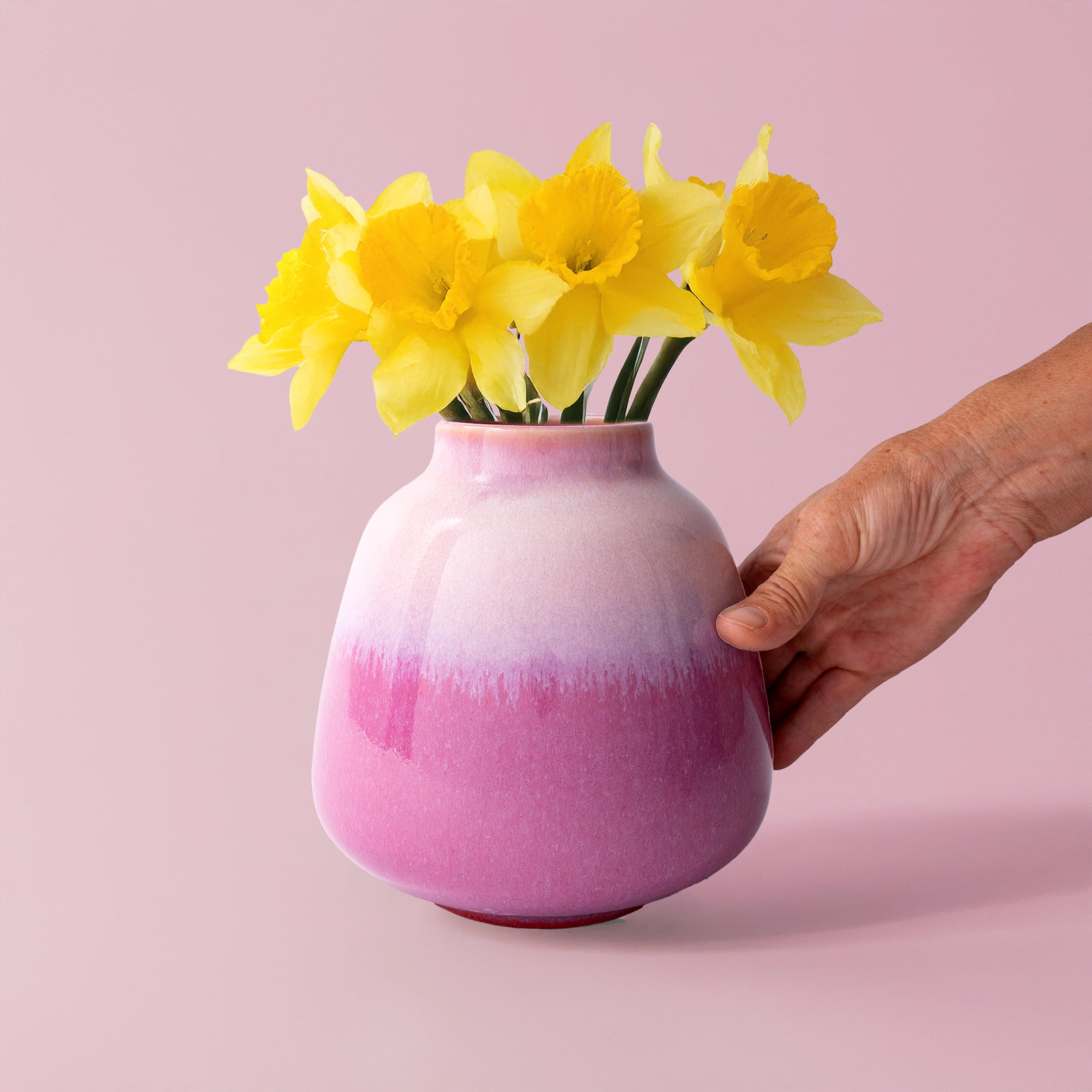 Pink gradient ceramic bouquet vase for home decor with yellow daffodils held by a hand