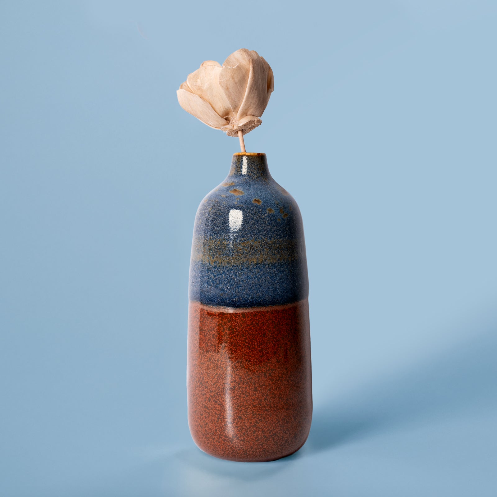 Pottery For The Planet eco-friendly home decor vase with blue and brown glaze holding a dried flower