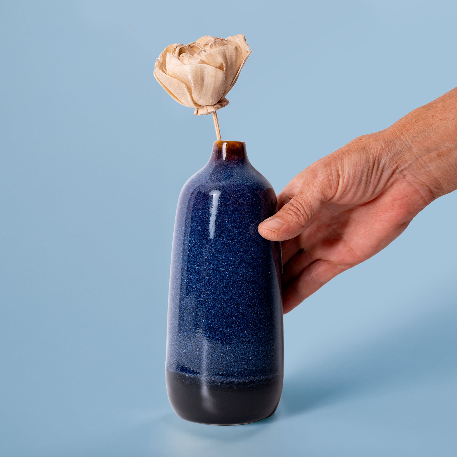 Hand holding blue and black eco-friendly home decor vase with dried flower by Pottery For The Planet