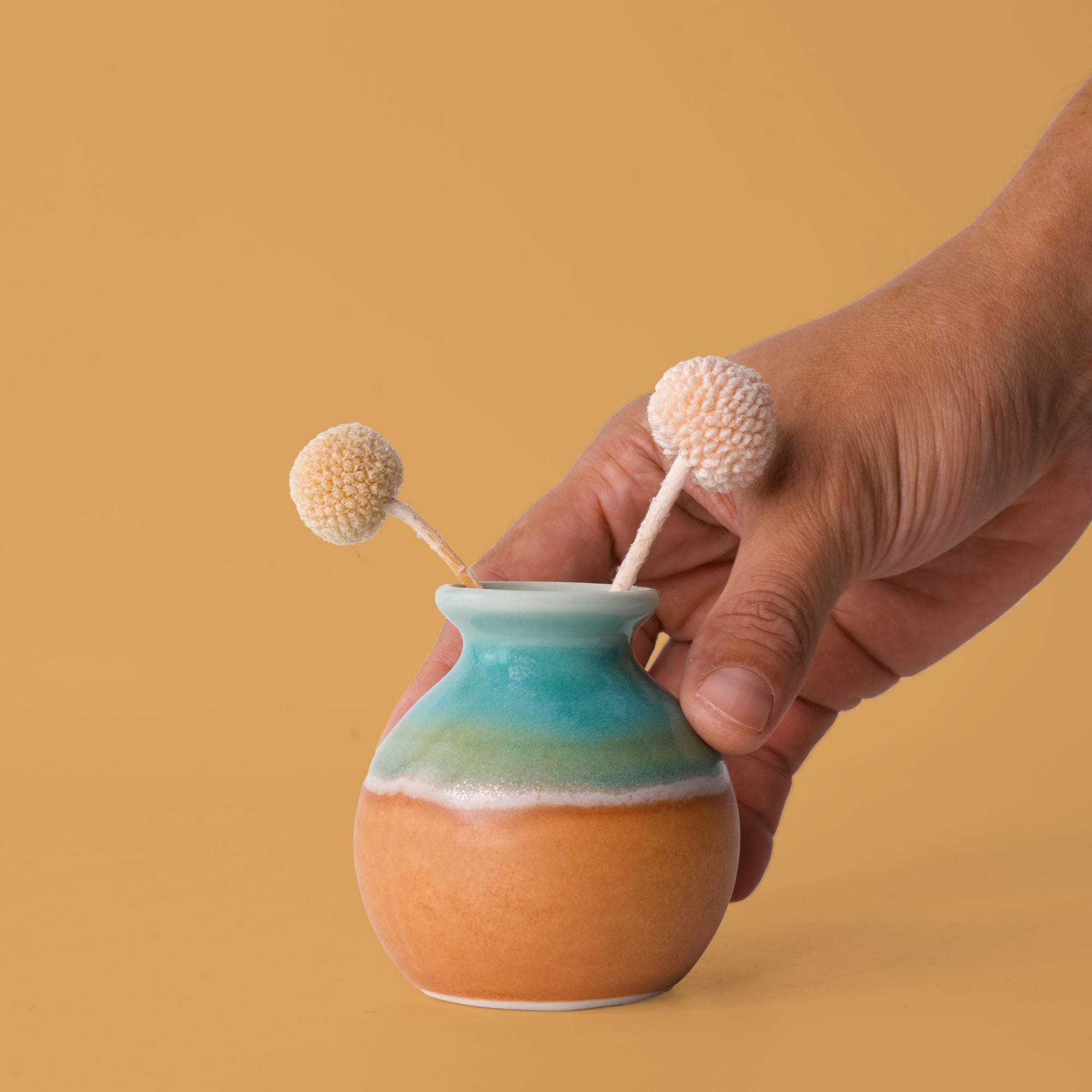 Hand holding a small eco-friendly home decor vase with blue and orange glaze from Pottery For The Planet