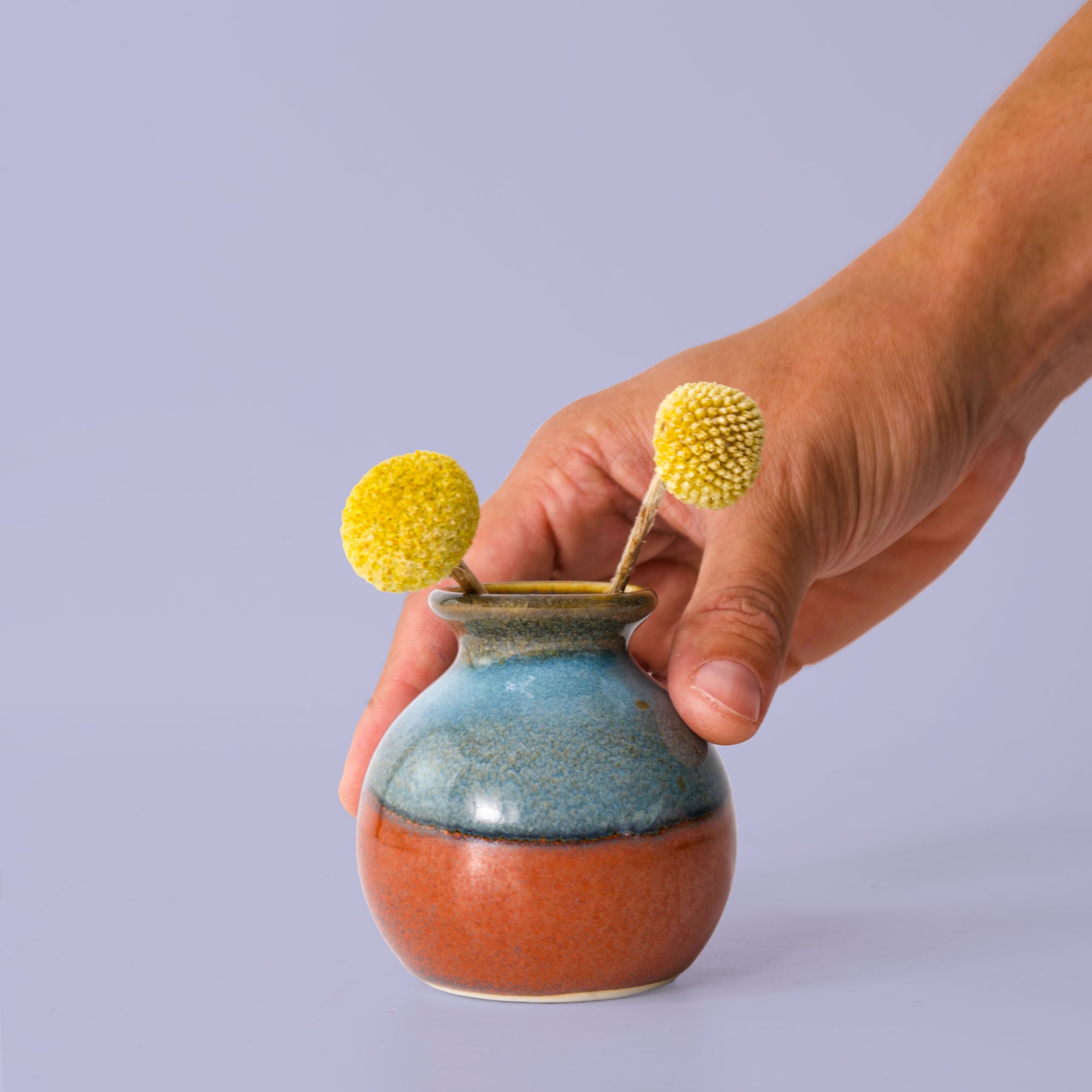 Hand holding a small blue and orange eco-friendly home decor vase with yellow flowers