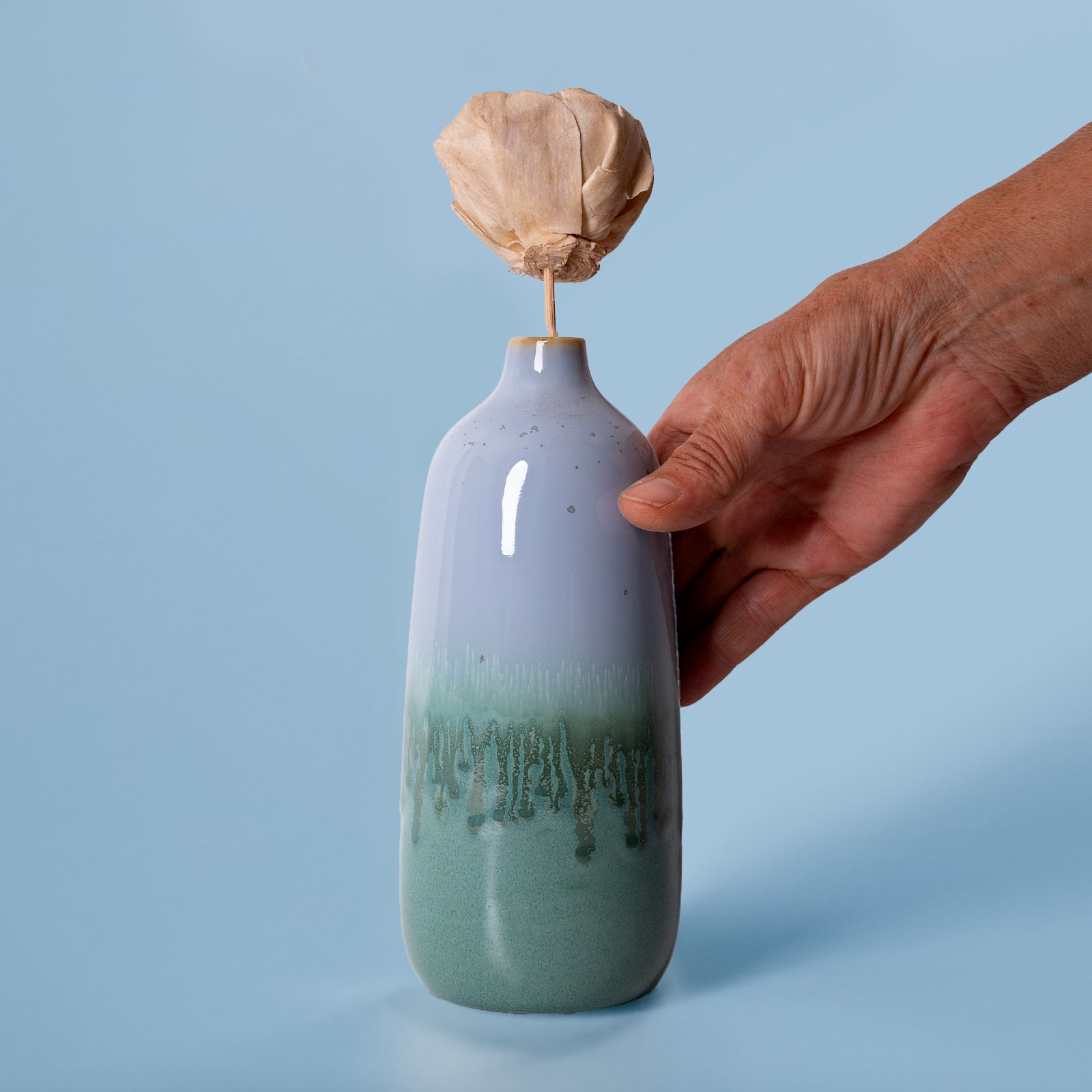 Hand holding eco-friendly home decor vase with blue and green glaze from Pottery For The Planet