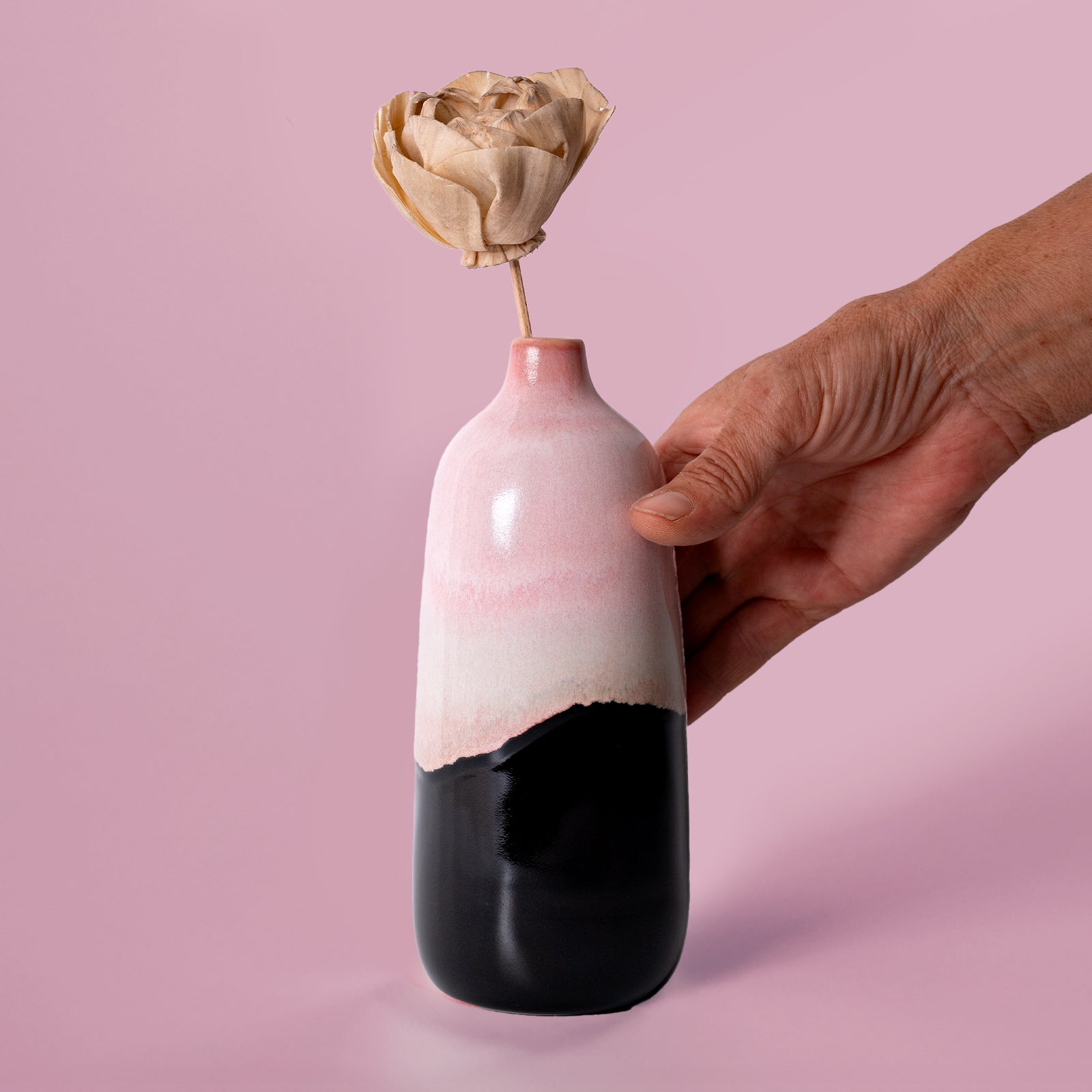 Hand holding Pottery For The Planet eco-friendly home decor vase with pink and black glaze and dried flower