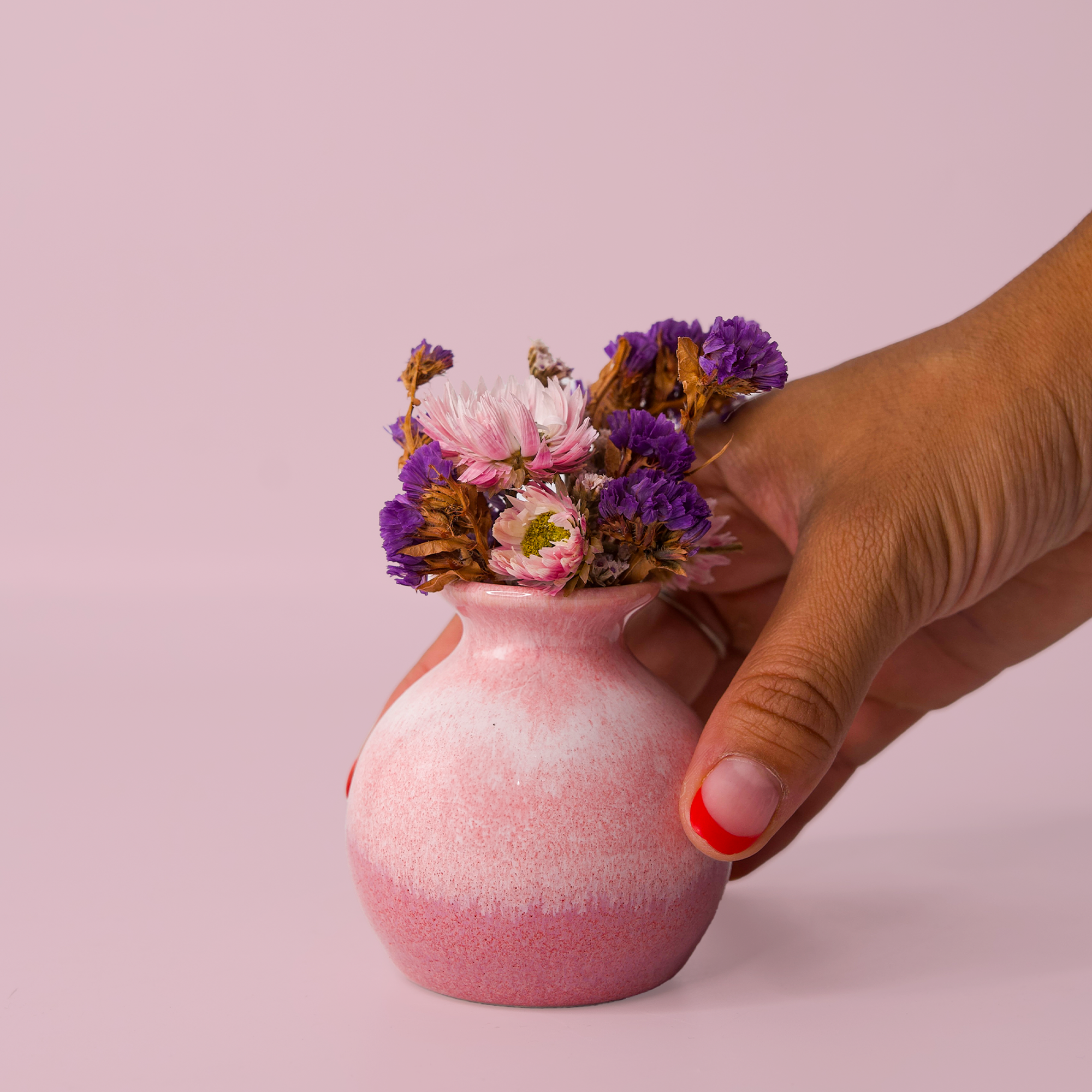Hand holding pink eco-friendly home decor vase with dried purple and pink flowers