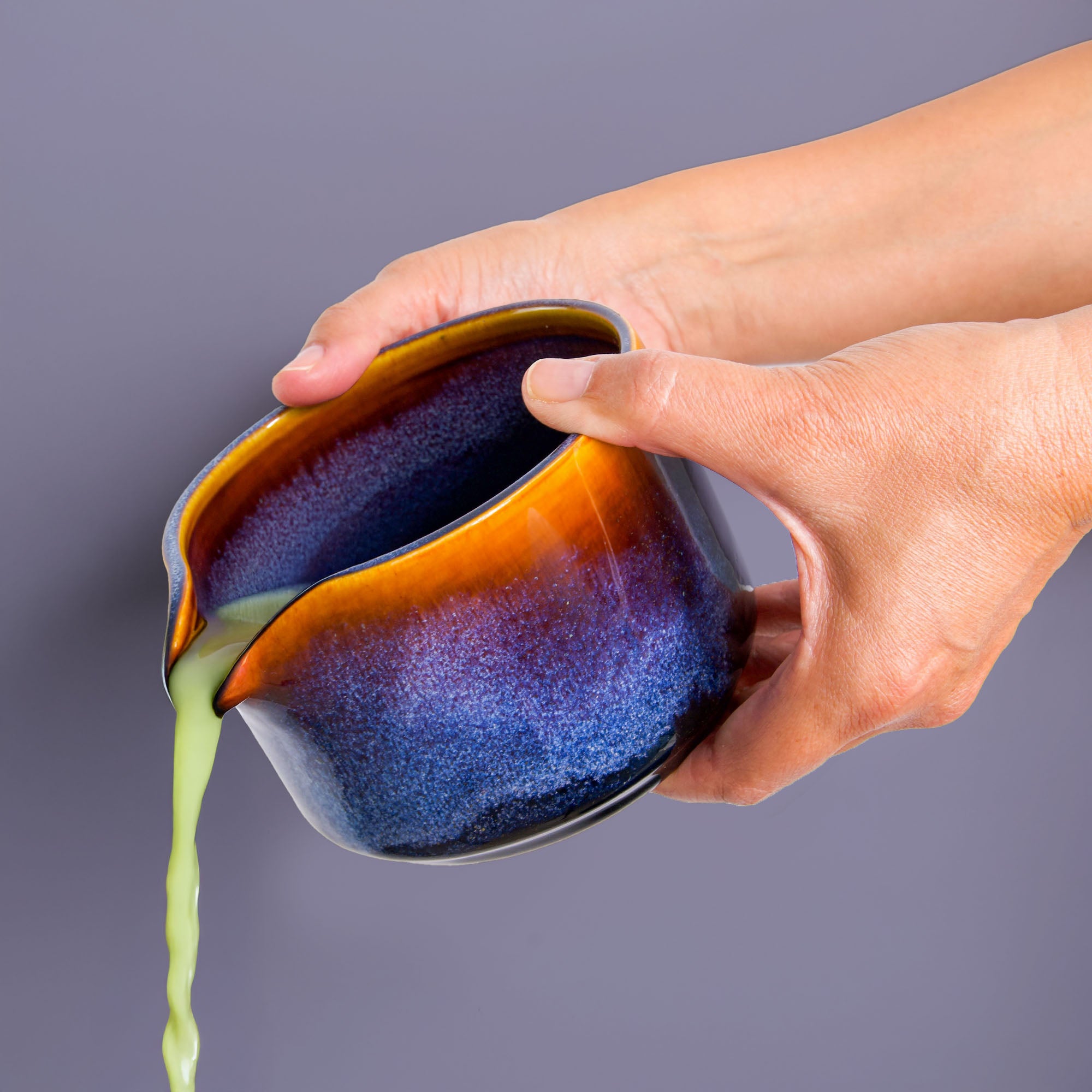 Hand pouring matcha tea from a handcrafted matcha bowl by Pottery For The Planet with blue and orange glaze