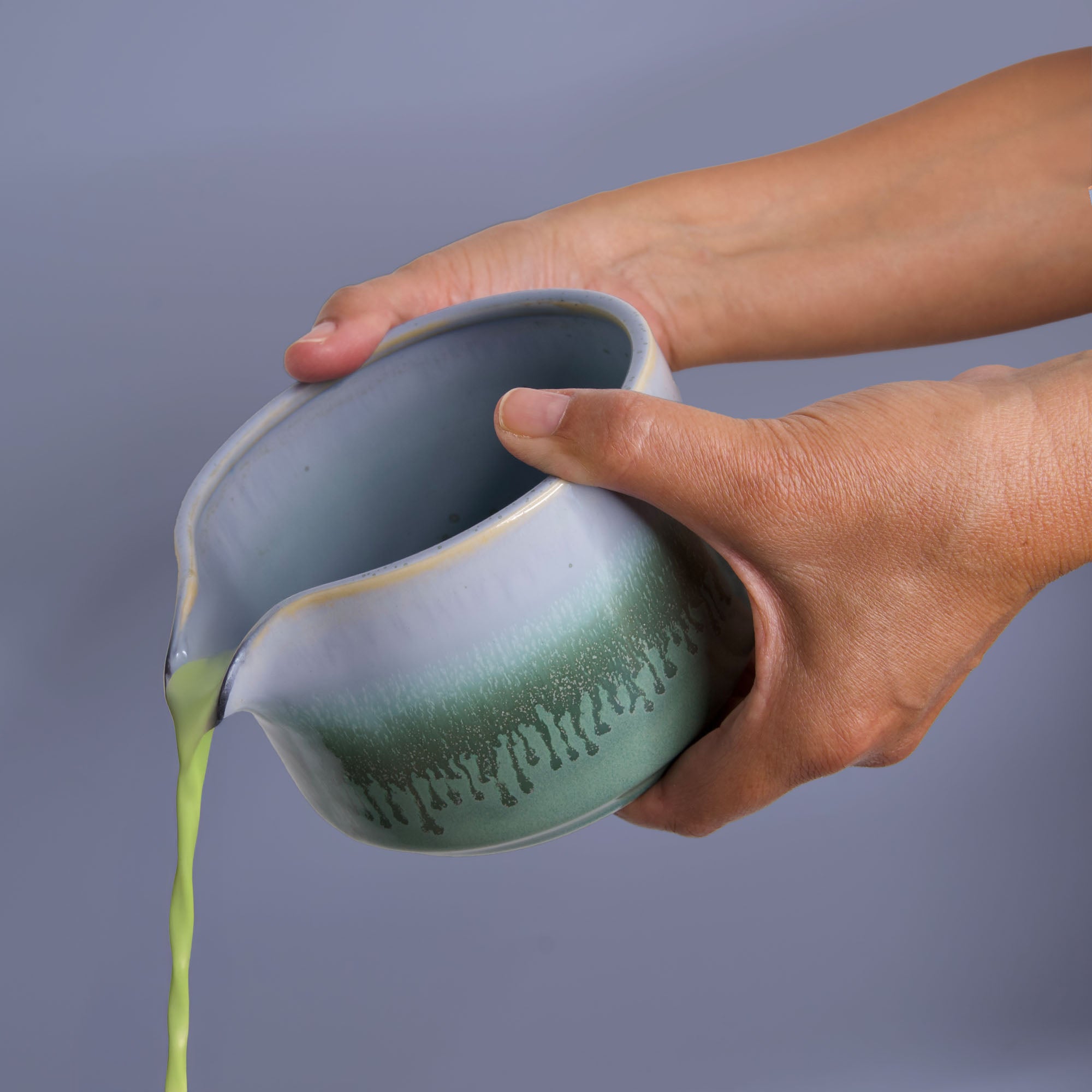 Hands pouring matcha from a handcrafted matcha bowl with green and white glaze by Pottery For The Planet