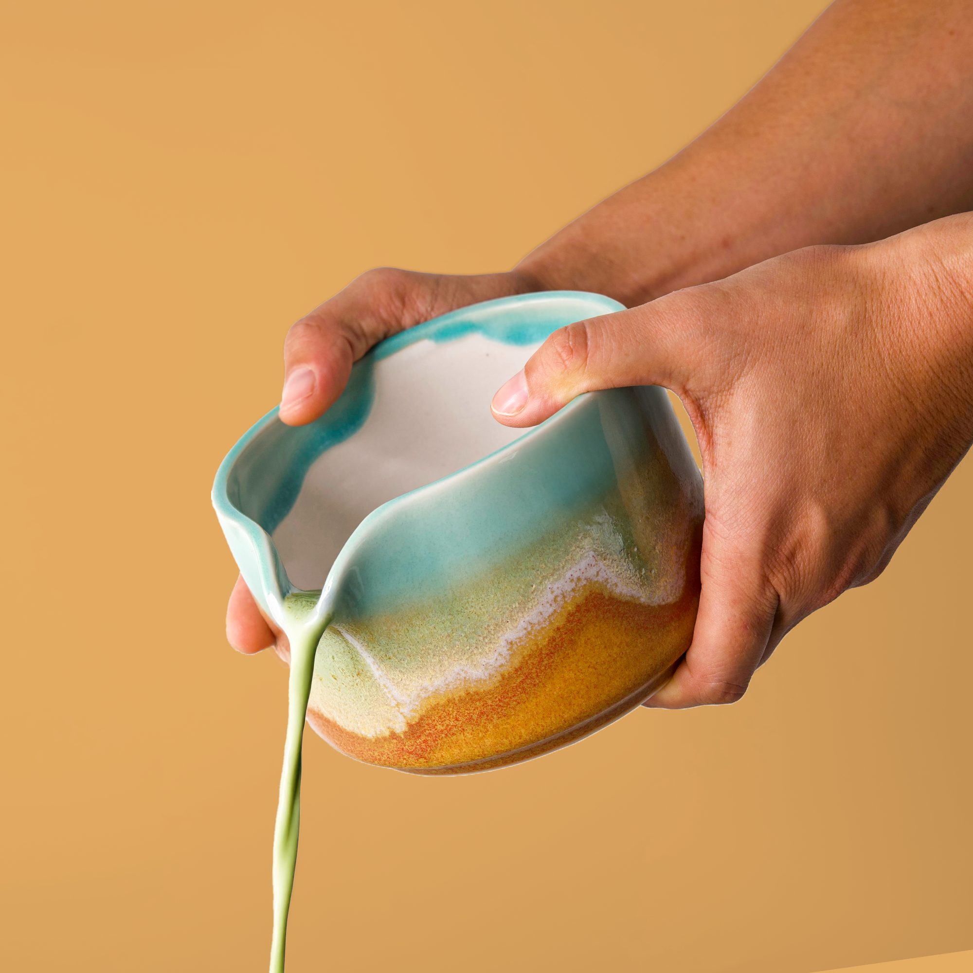 Hand pouring tea from a handcrafted matcha bowl with turquoise and earthy glaze by Pottery For The Planet