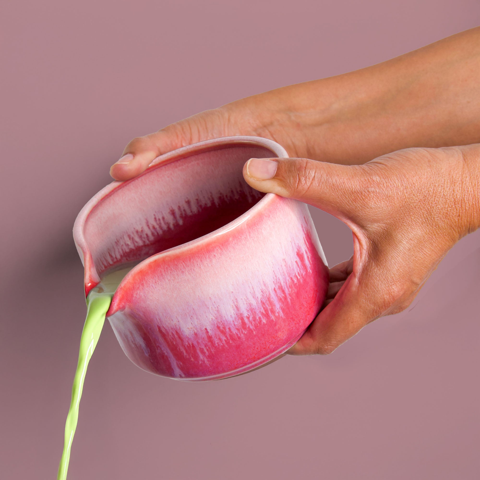 Hand pouring matcha tea from a handcrafted matcha bowl with red and white glaze by Pottery For The Planet