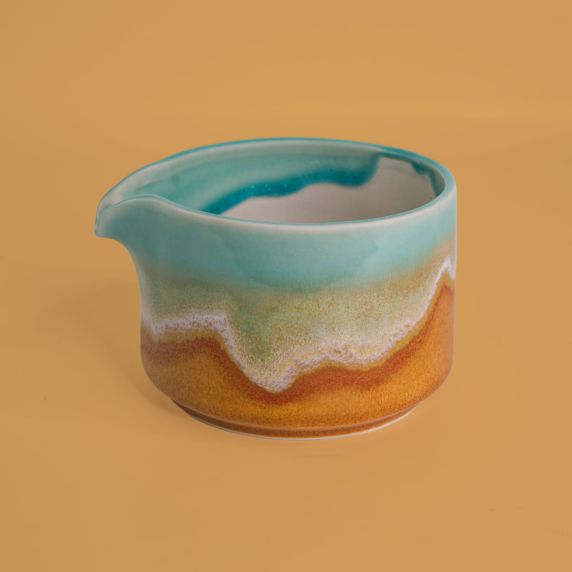 Pottery For The Planet handcrafted matcha bowl with turquoise and earthy glaze on a beige background
