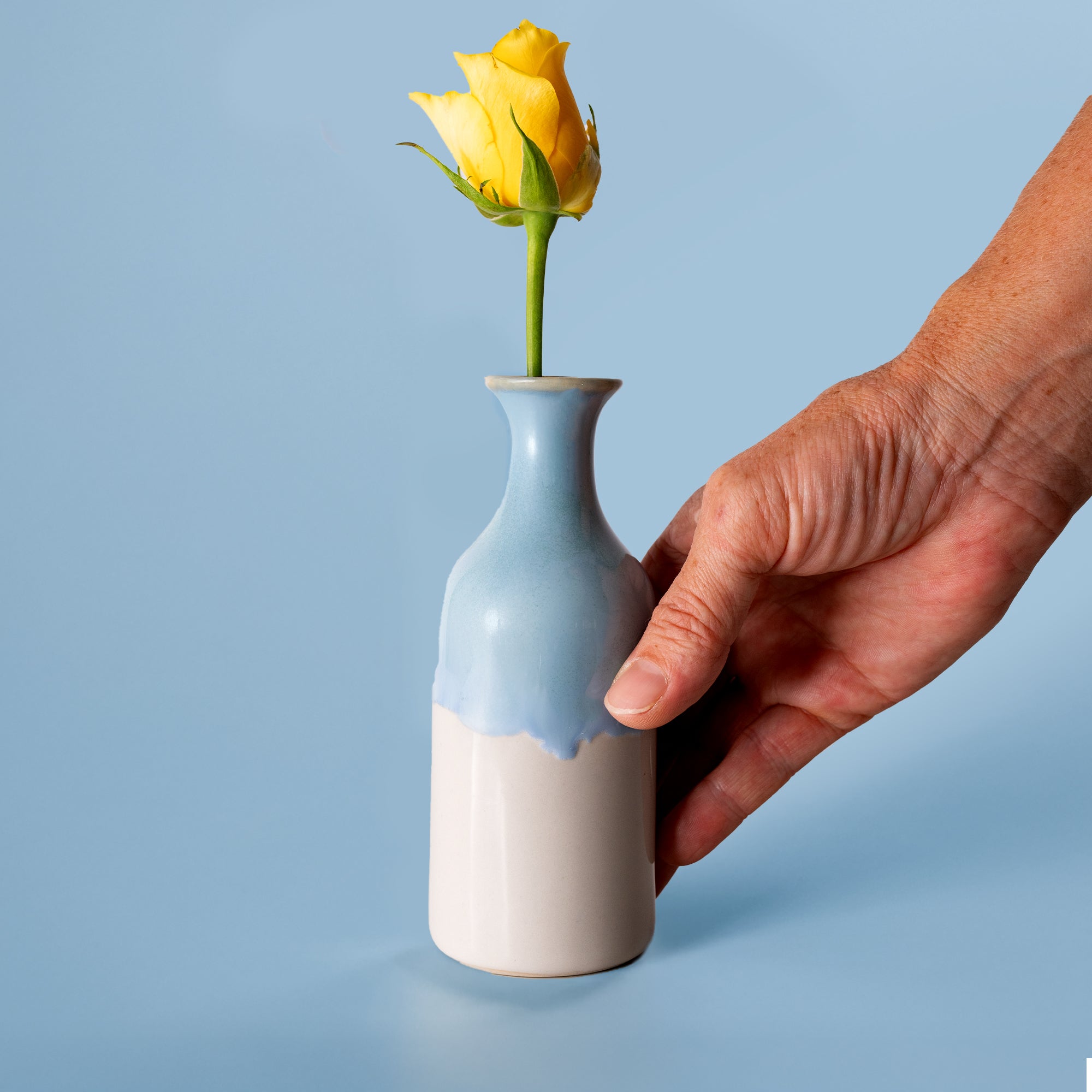 Small handmade flower vase in blue and white held by hand with a yellow rose inside